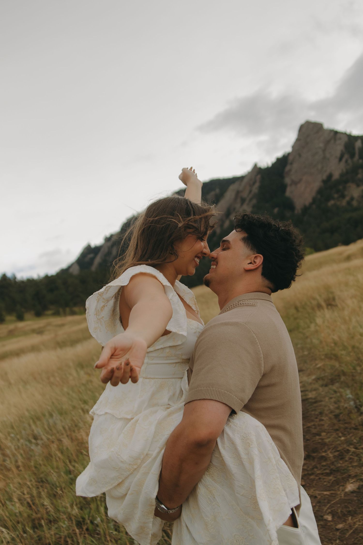 Couple sharing a joyful moment in a golden field with rocky Flatirons mountains in the background.