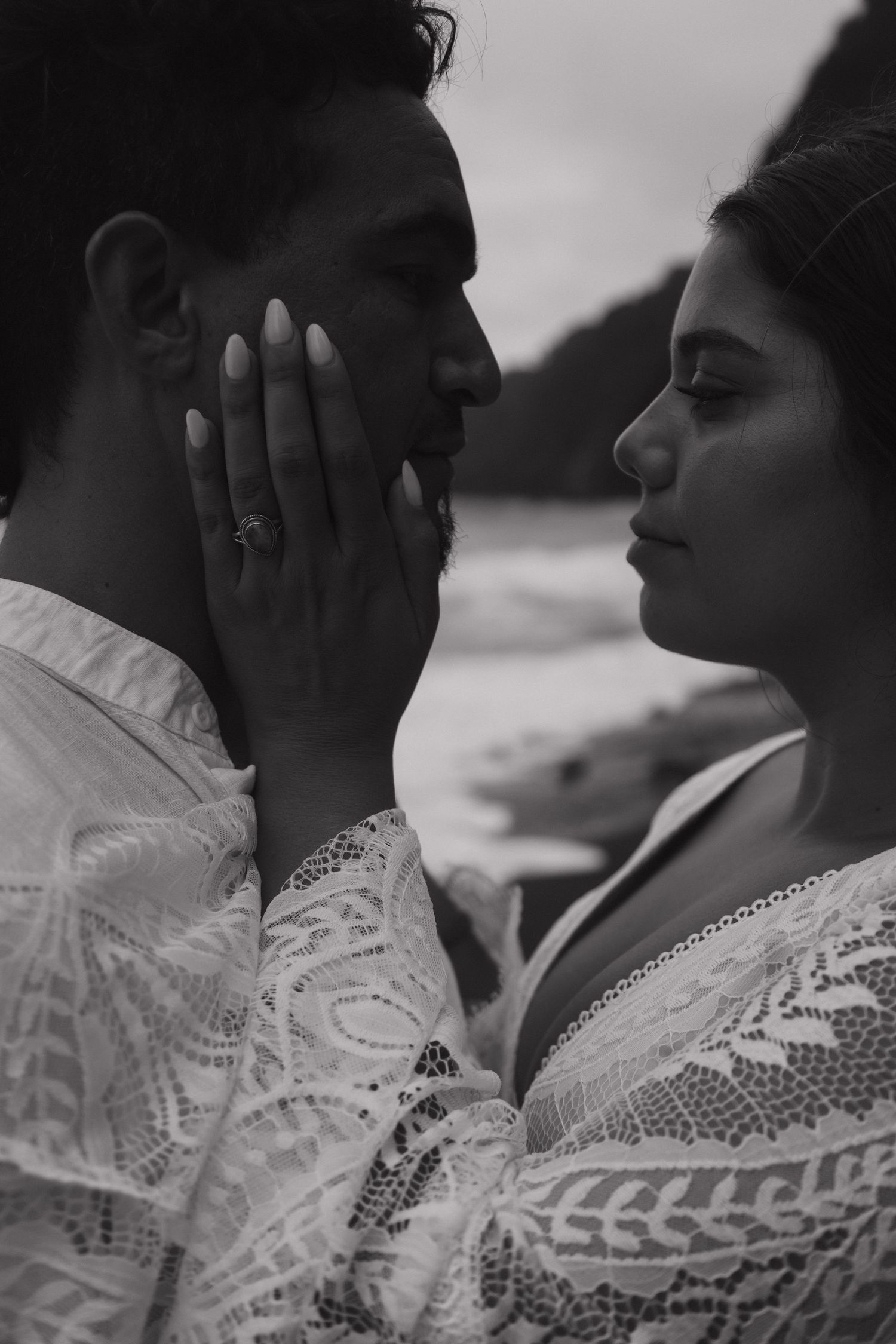 Black and white close-up of bride tenderly cupping grooms face with engagement ring visible.