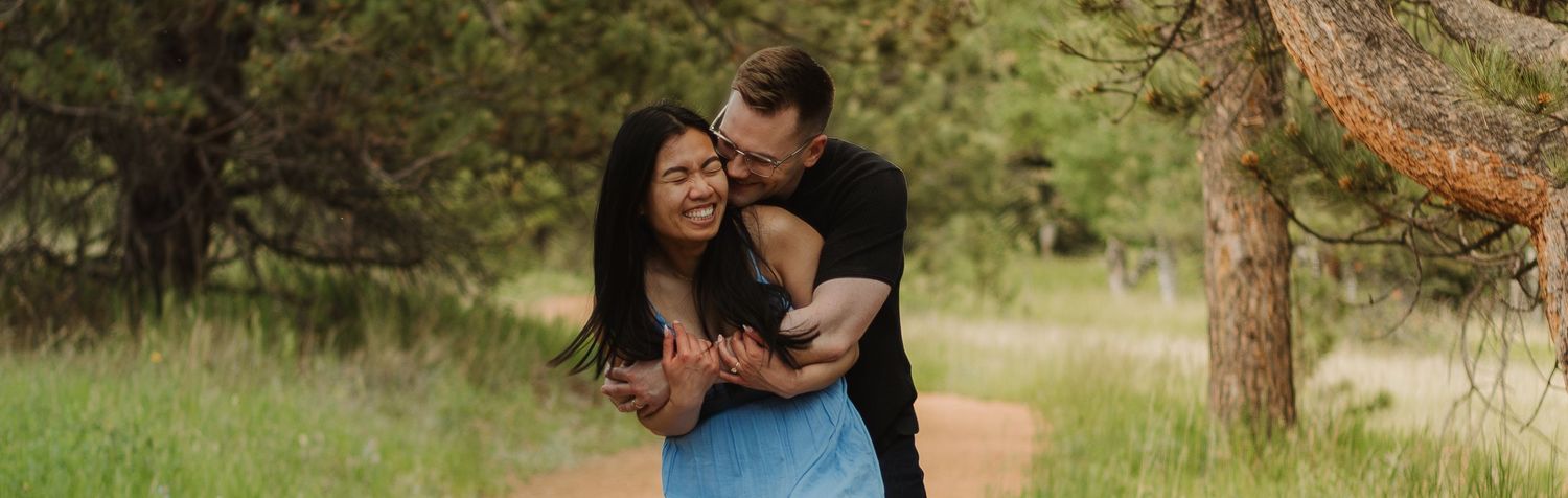 A romantic embrace on a nature trail with pine trees in the background.