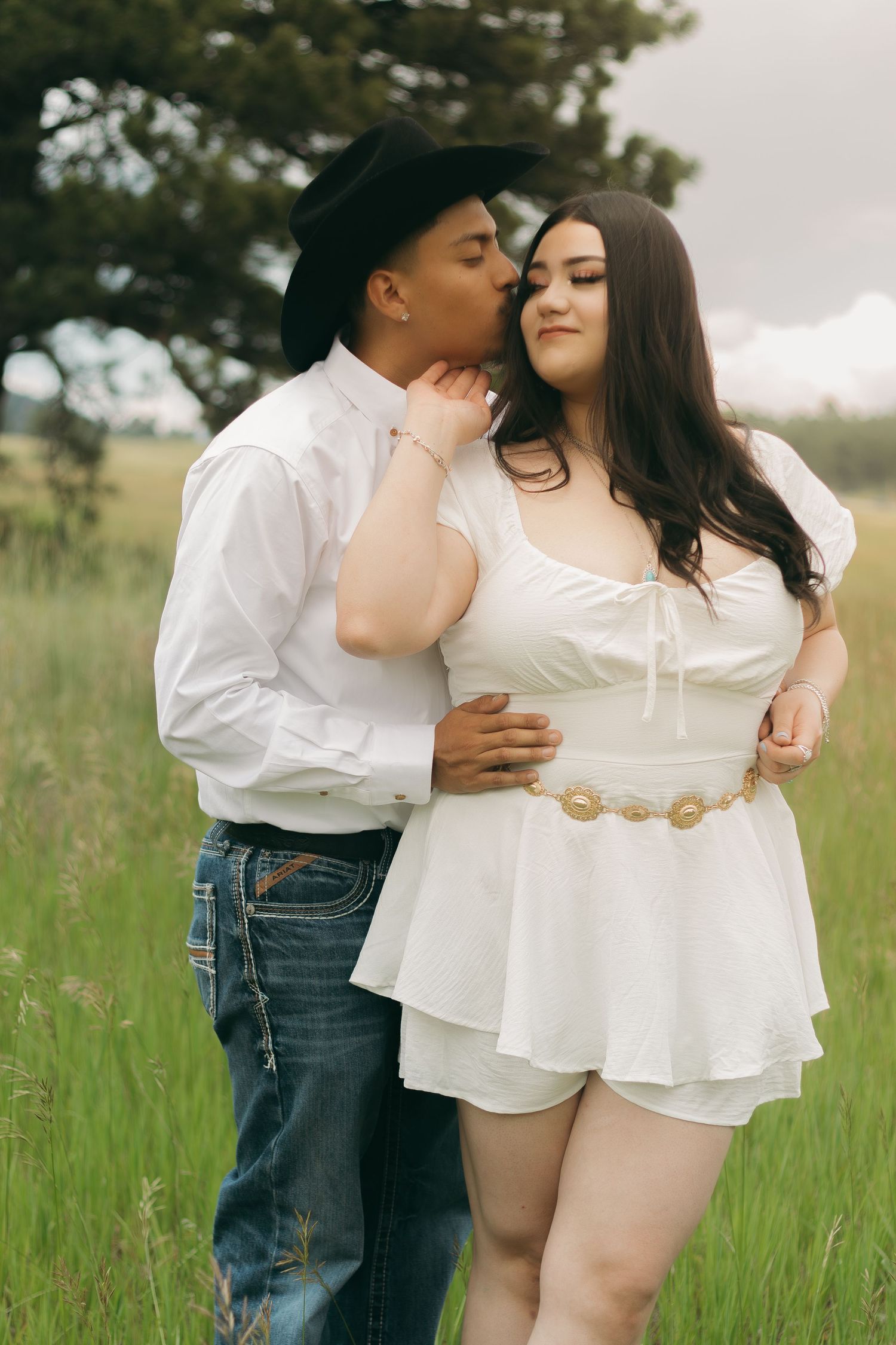 Couple in white clothing sharing tender moments in a sunny meadow.