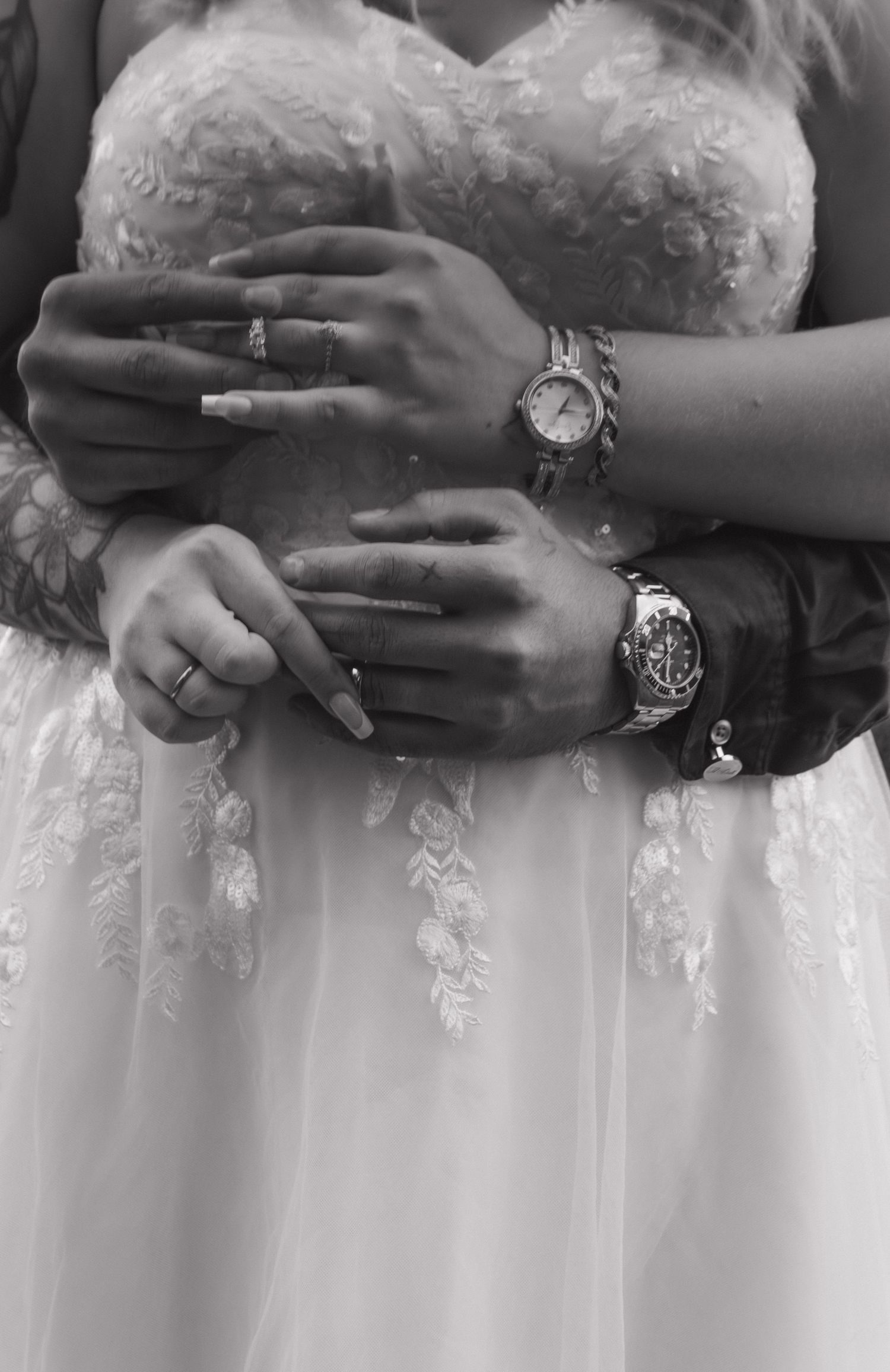 Close-up detail of hands embracing around a white wedding dress with lace detailing.