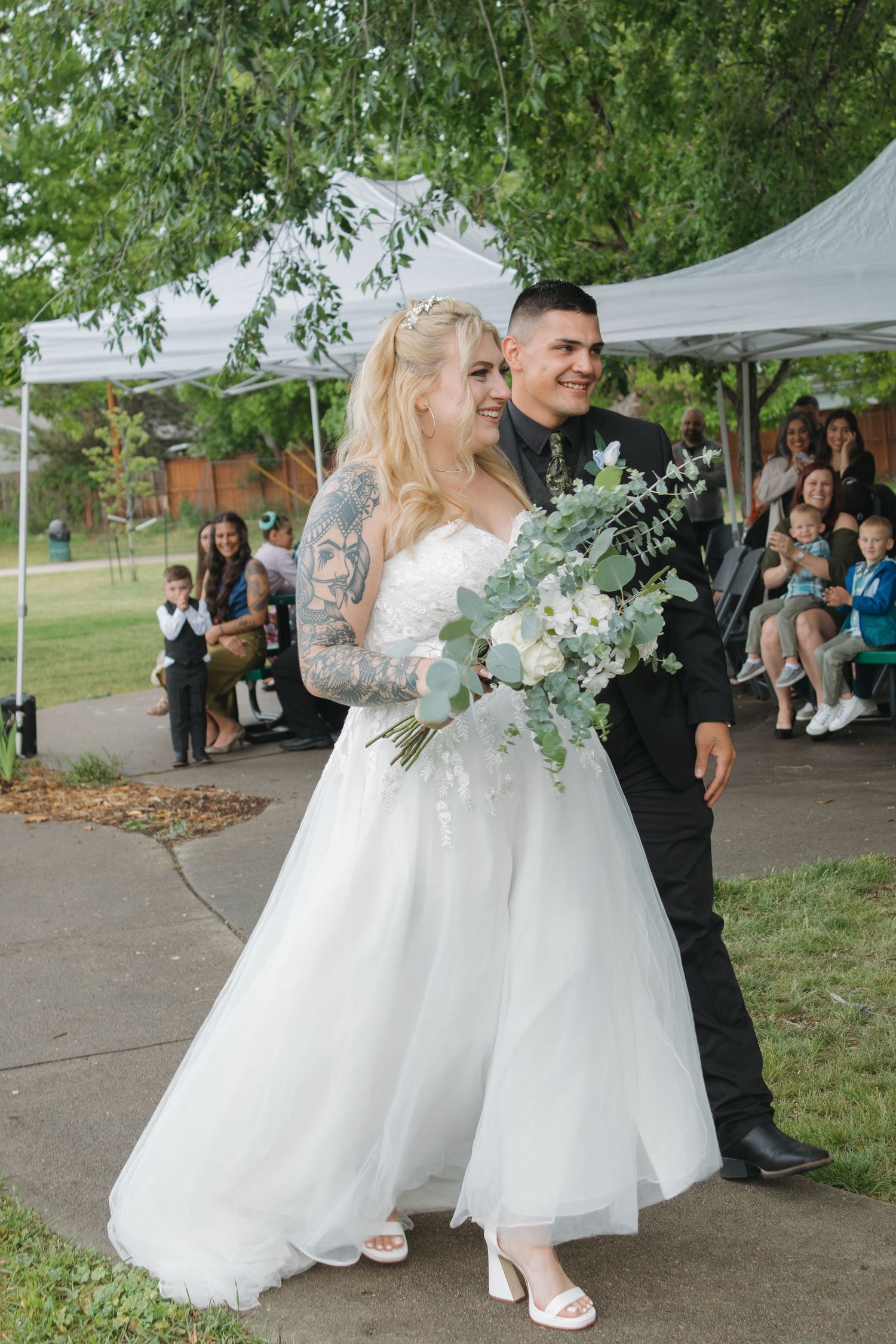 Wedding couple sharing intimate moments while guests look on during outdoor reception.
