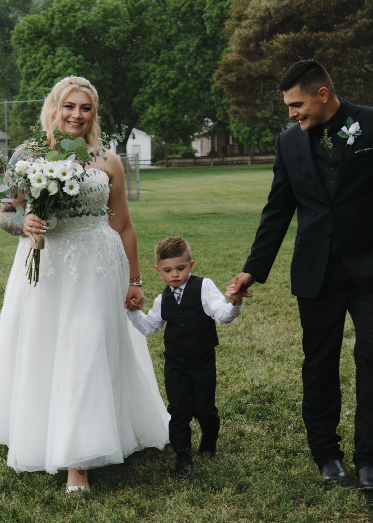 Sweet moment between wedding couple and young ring bearer on grassy field.