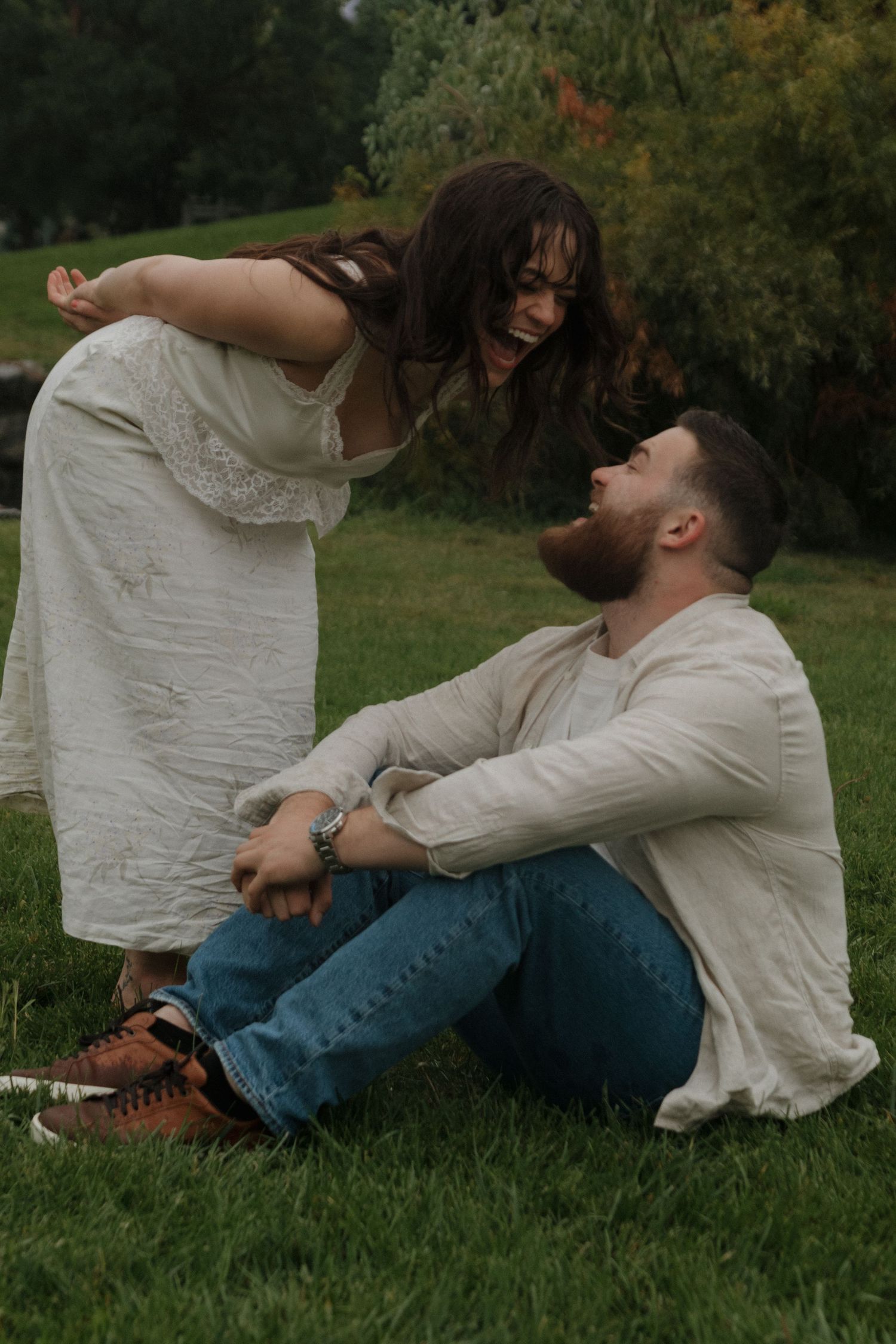 Two people in white clothing share a playful moment while sitting on green grass.