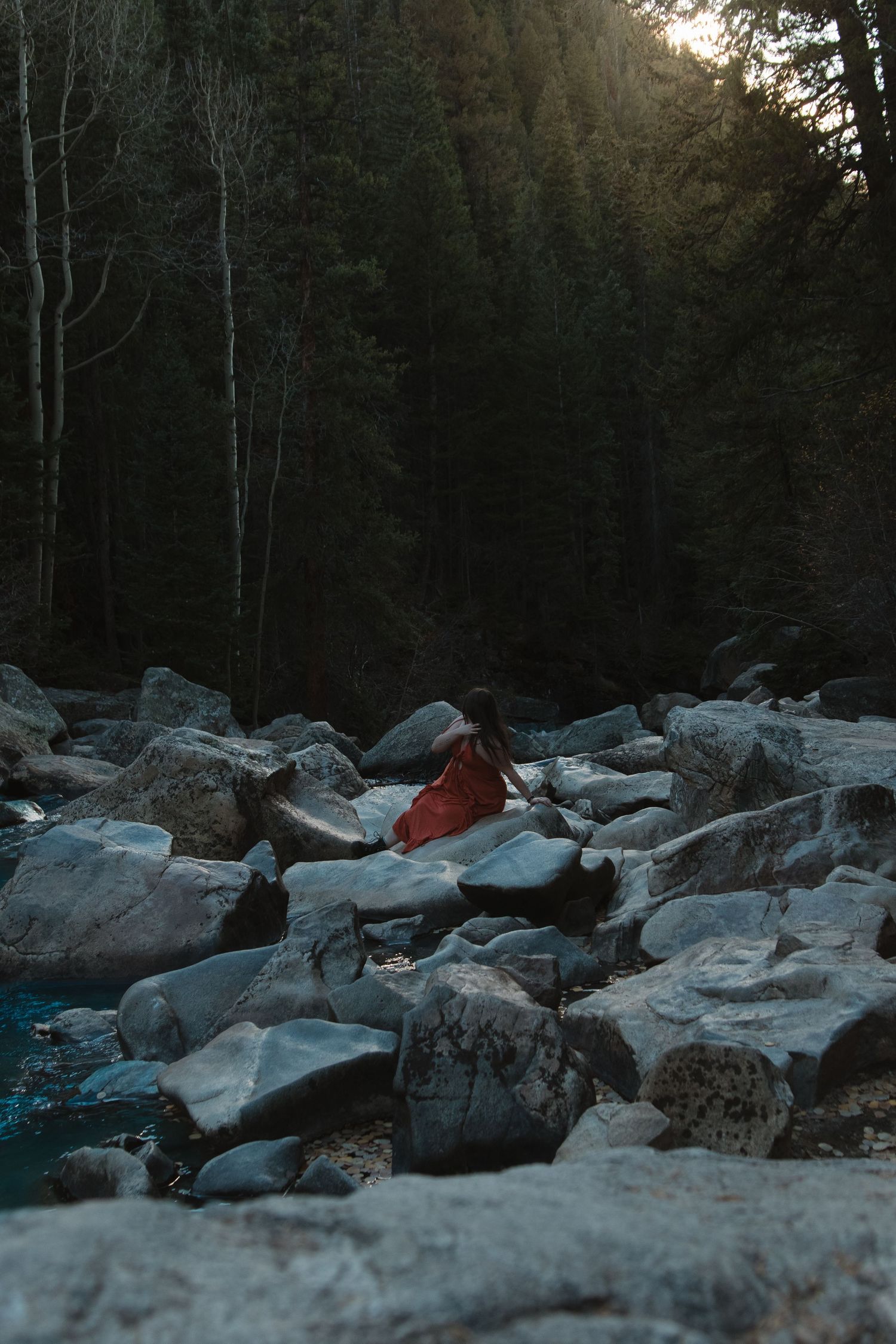 A rocky river bed with large boulders and forest trees in the background during dusk.