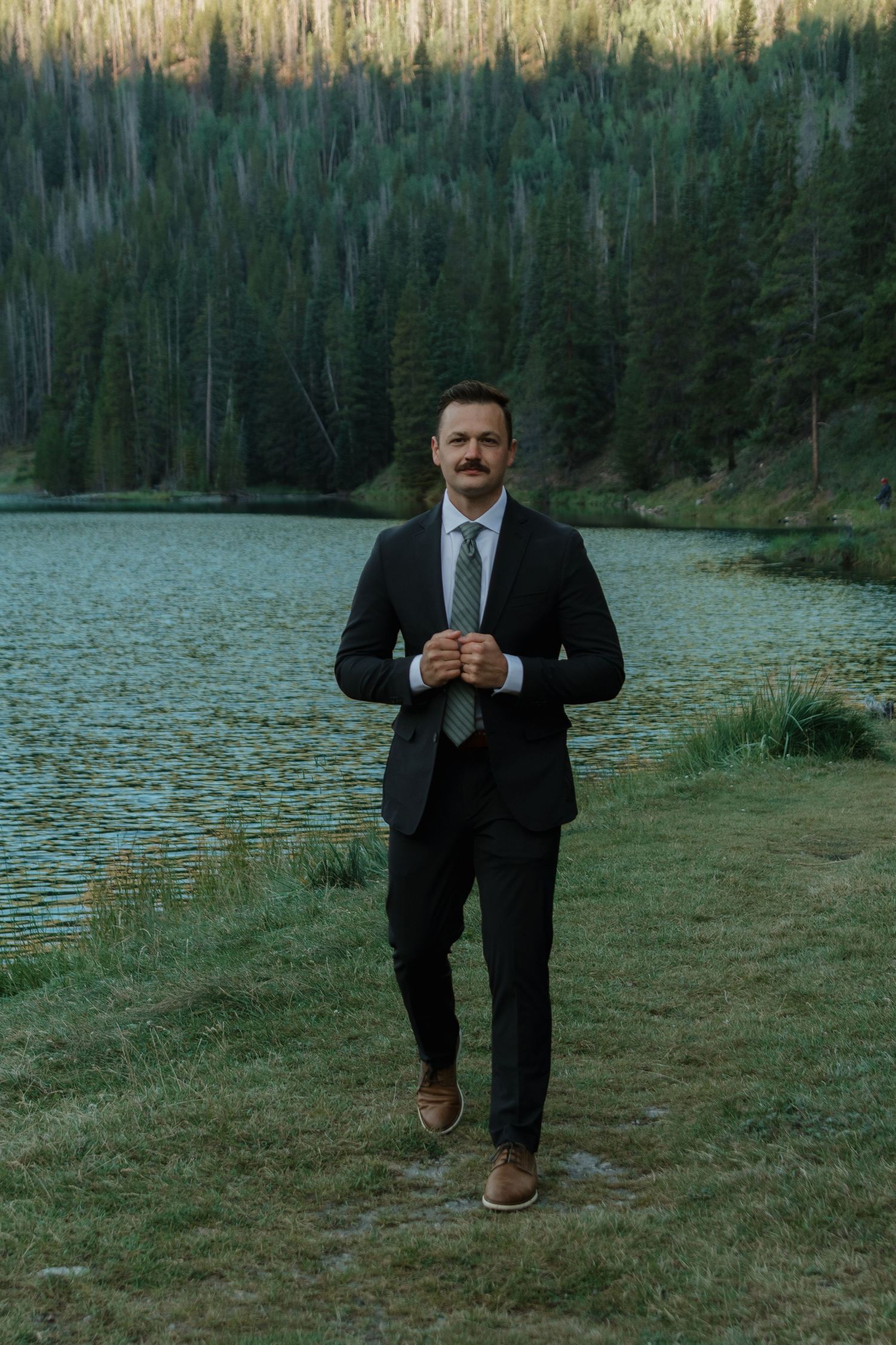 A series of playful poses in a black suit against a serene lake and forest backdrop.
