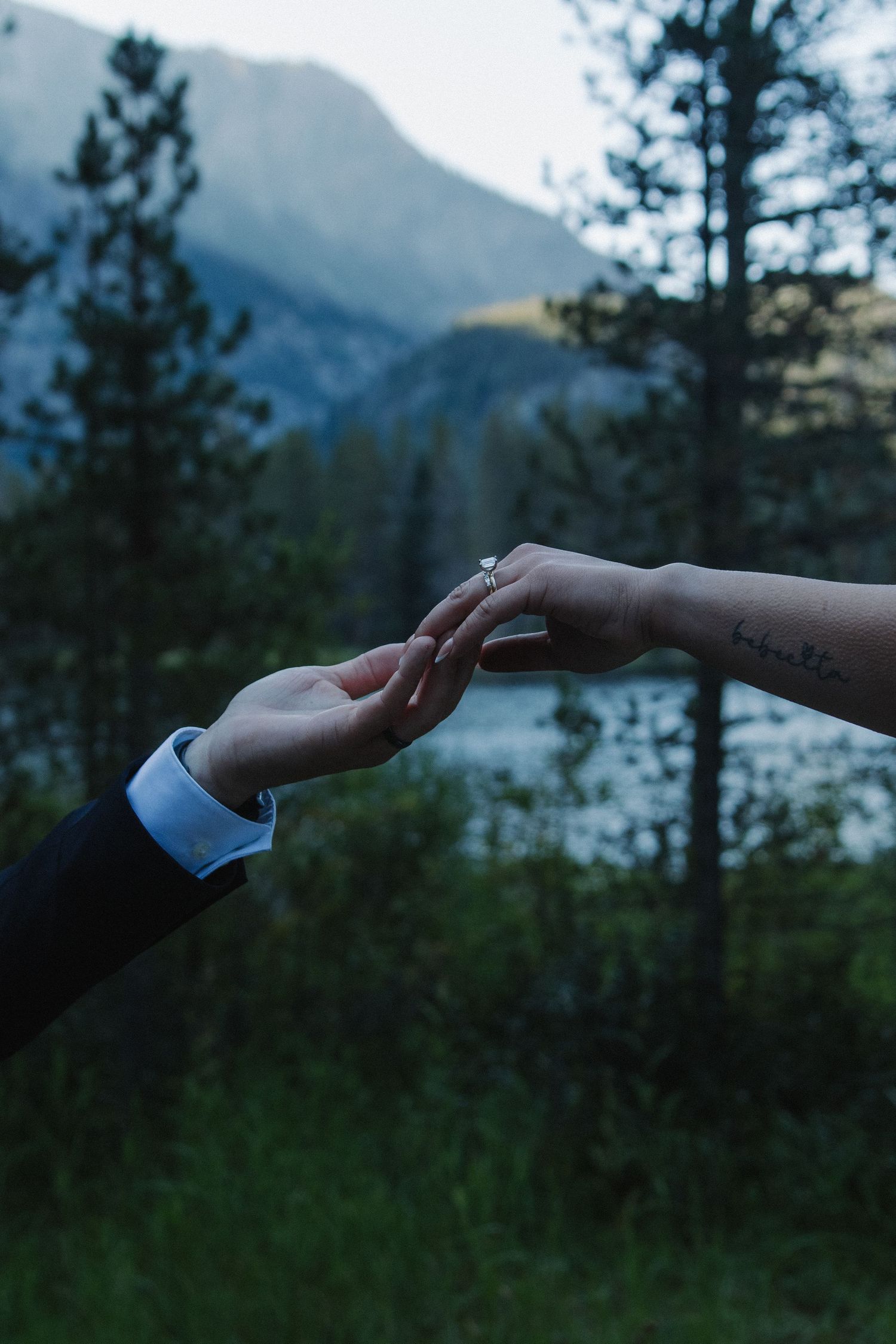Gentle hands reaching toward each other with mountains and lake in the background.