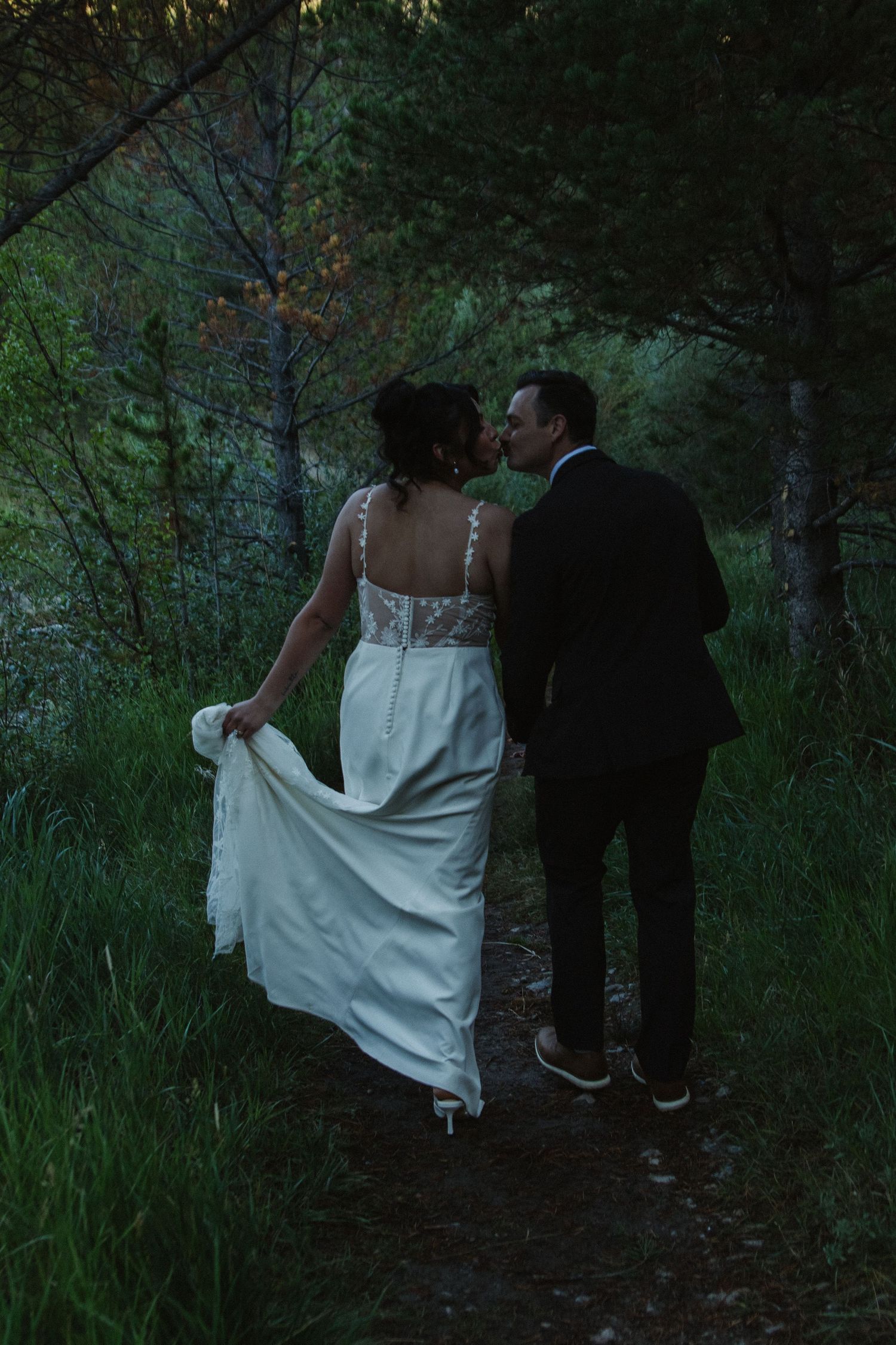 A couple walking through tall grass on a forested path at dusk.