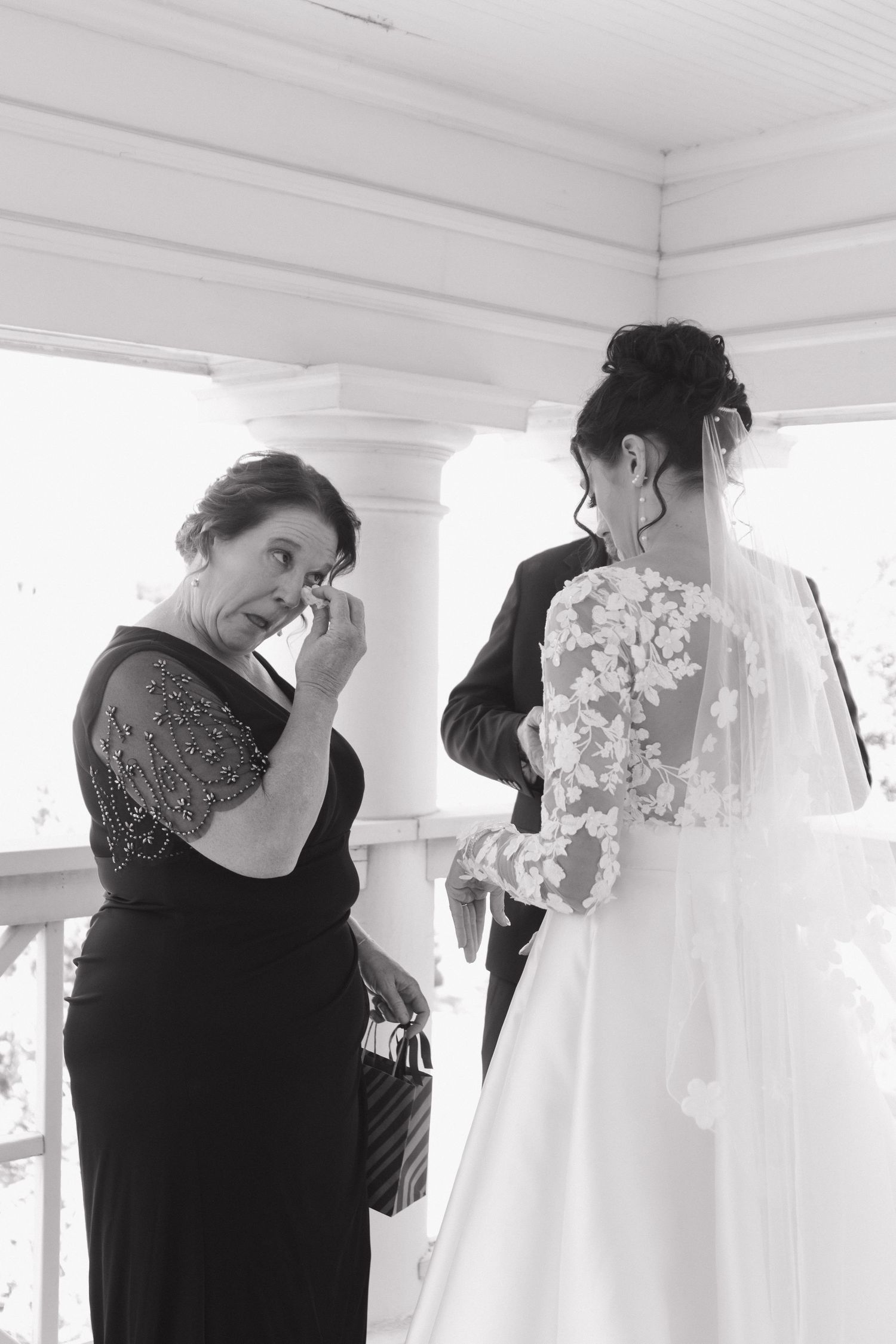 Woman in black dress examines white wedding gowns hanging on display in a bright room.