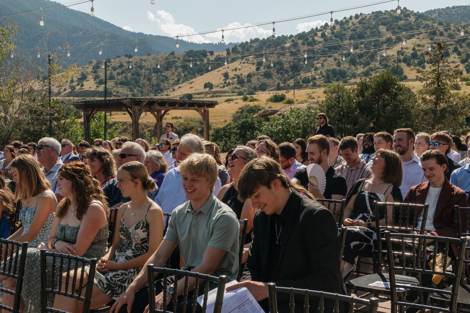 Large crowd of wedding guests gathered at an outdoor mountain venue.