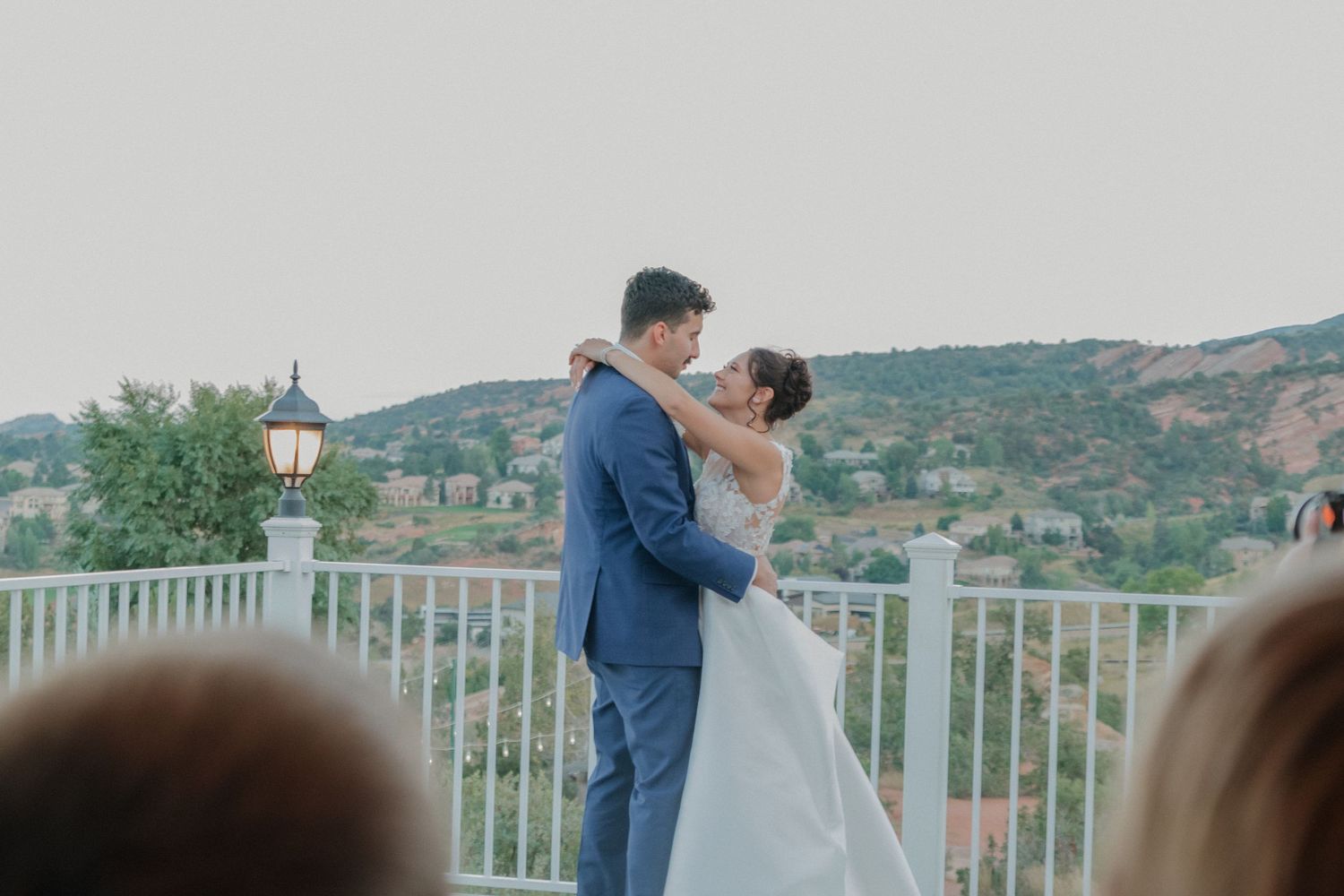 Wedding couple shares romantic moment on balcony overlooking mountain landscape.