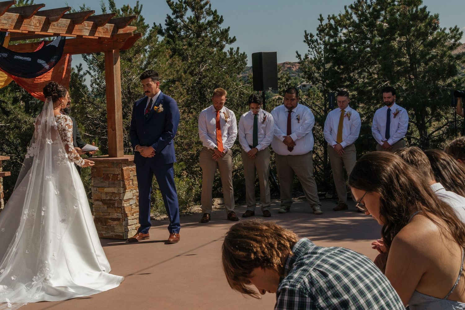 Wedding ceremony setup outdoors with rows of chairs and standing guests.