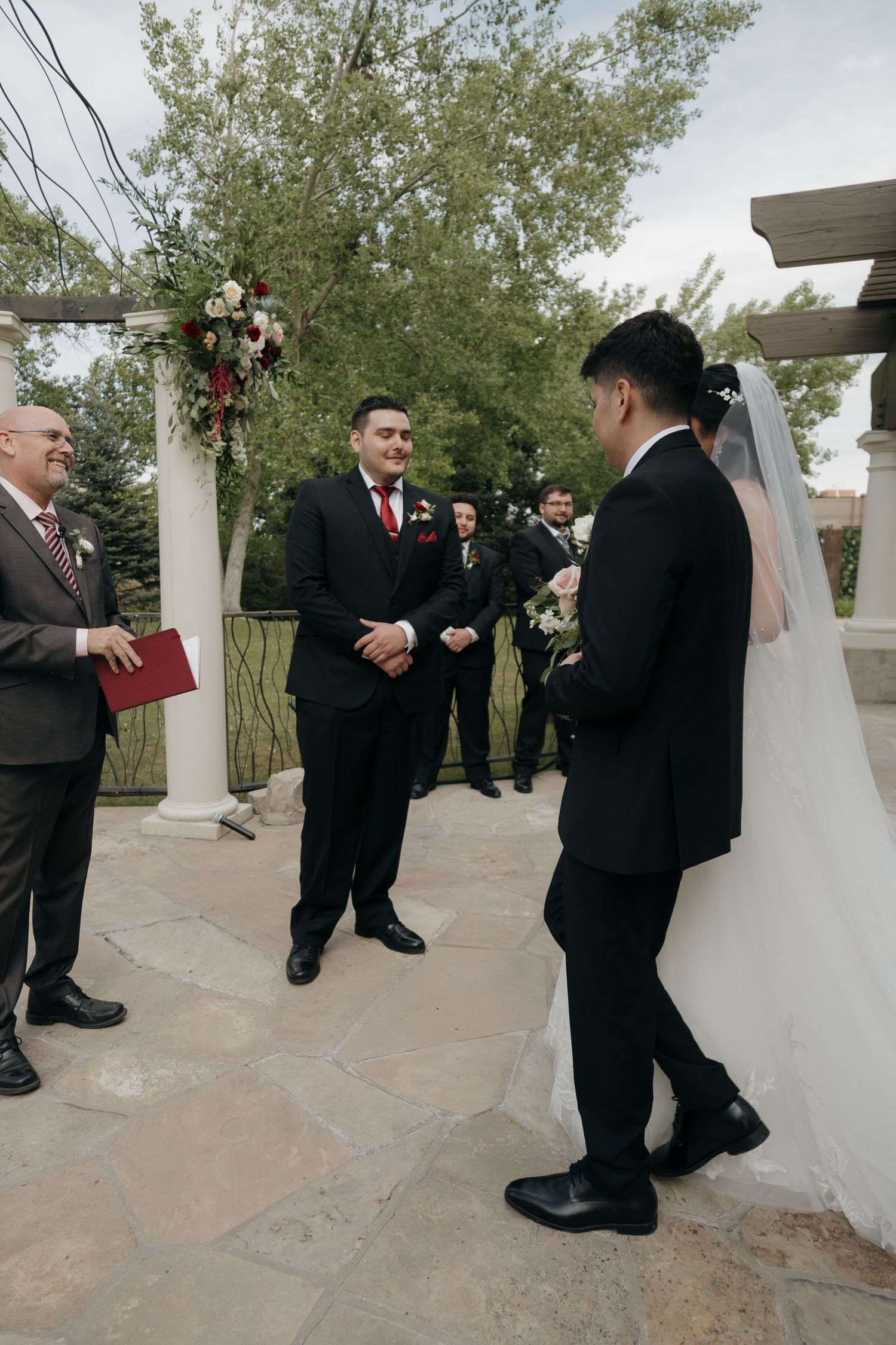 Groom smiles as bride is walked down the aisle at an outdoor wedding ceremony.