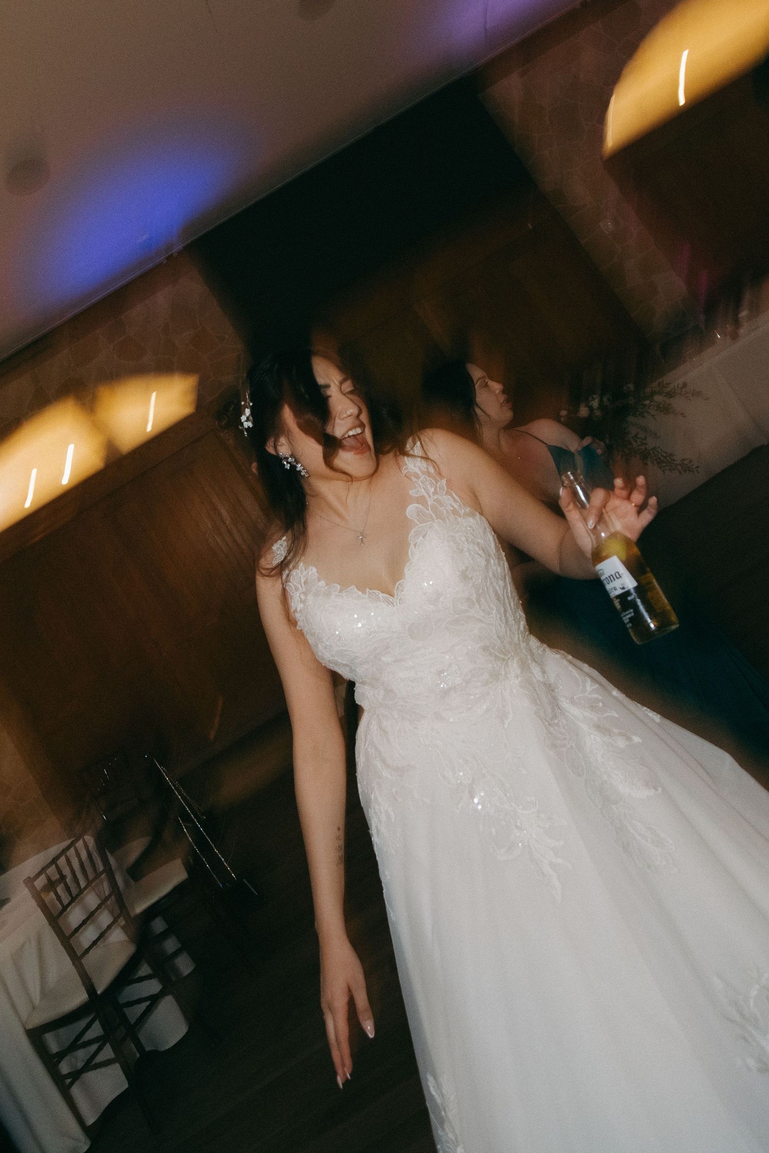 Bride in lace gown dancing with a drink at her wedding reception.
