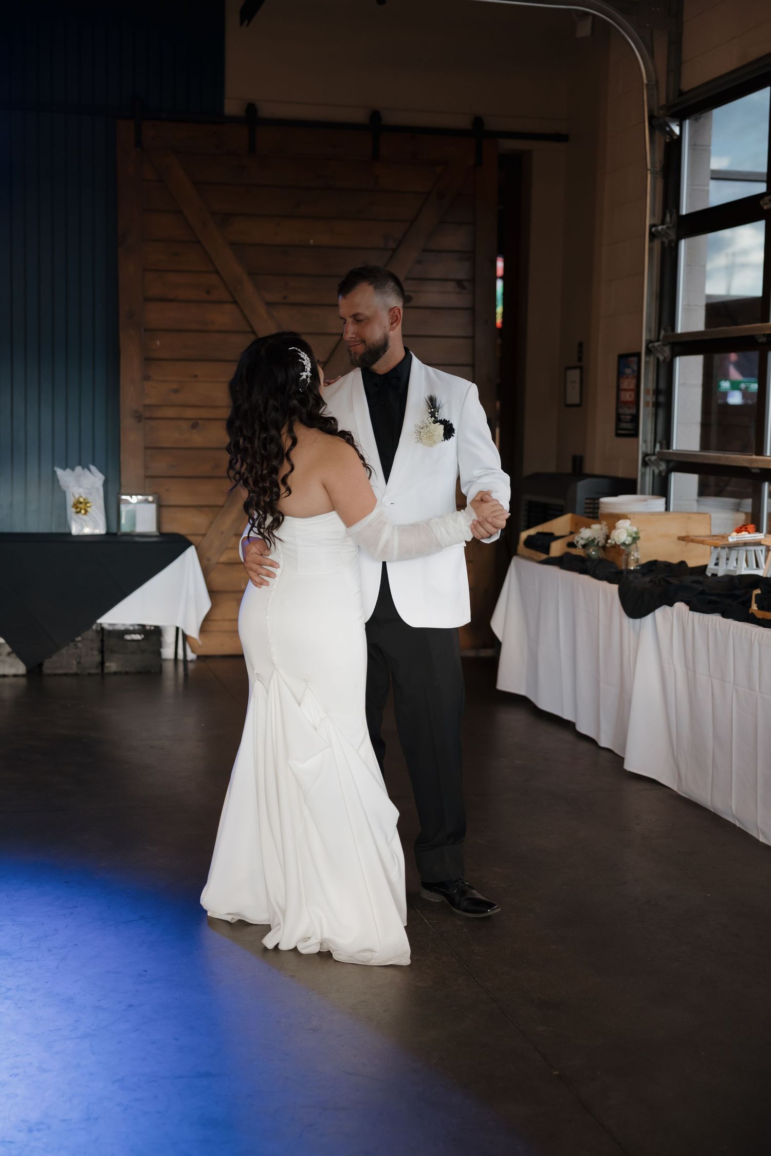 Bride and groom share romantic first dance in rustic barn venue with sliding wood doors.