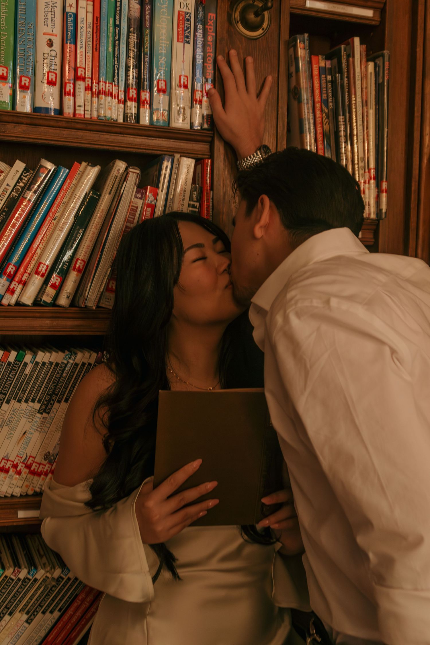 Romantic couple sharing intimate moments against a backdrop of library books in warm lighting.