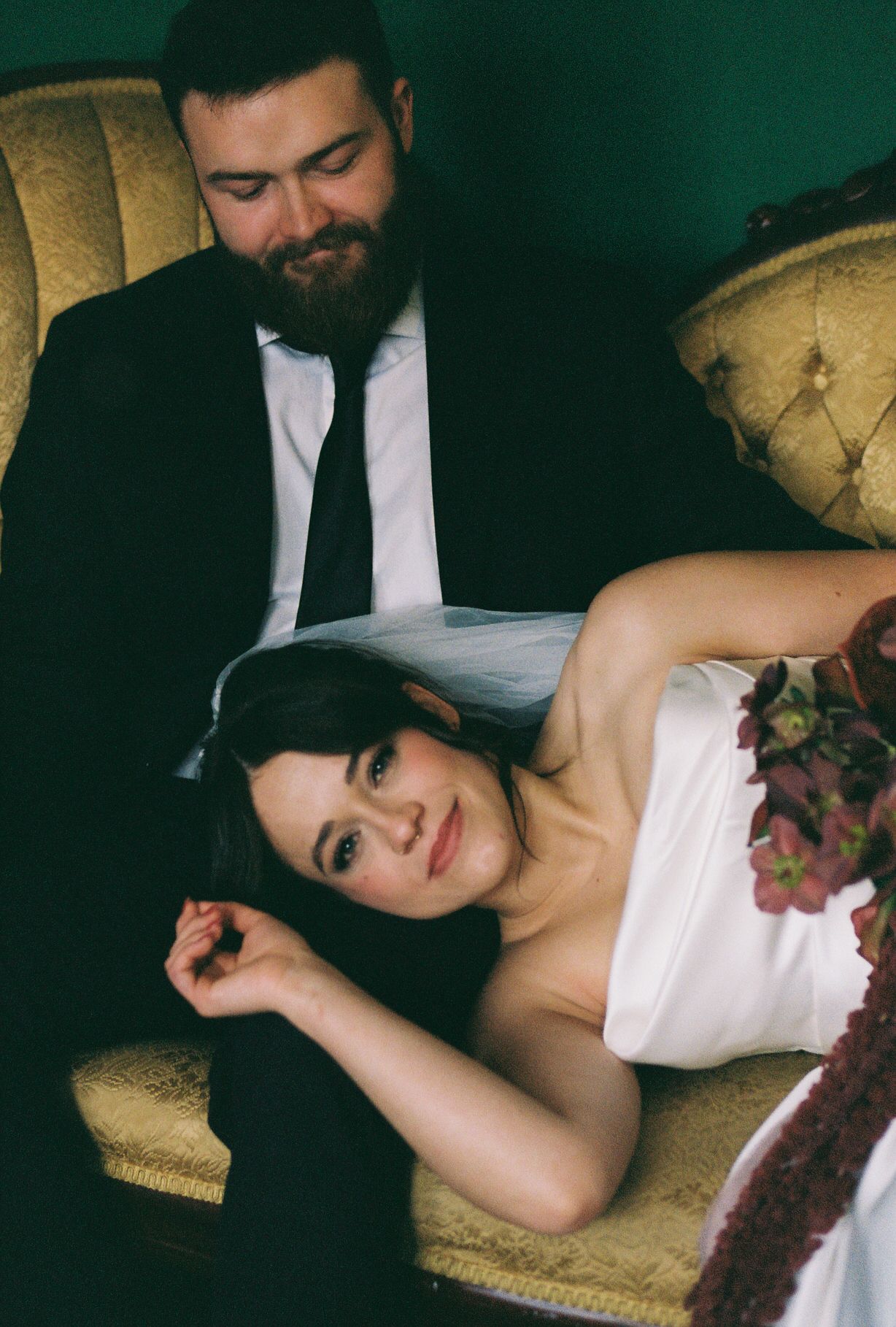 A couple relaxing together on a vintage gold tufted chair in formal attire.