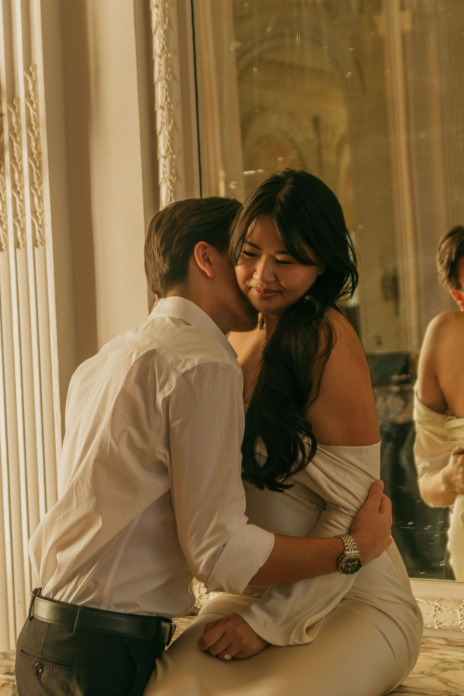 A romantic couple embraces in an elegant room with ornate white columns and warm lighting.