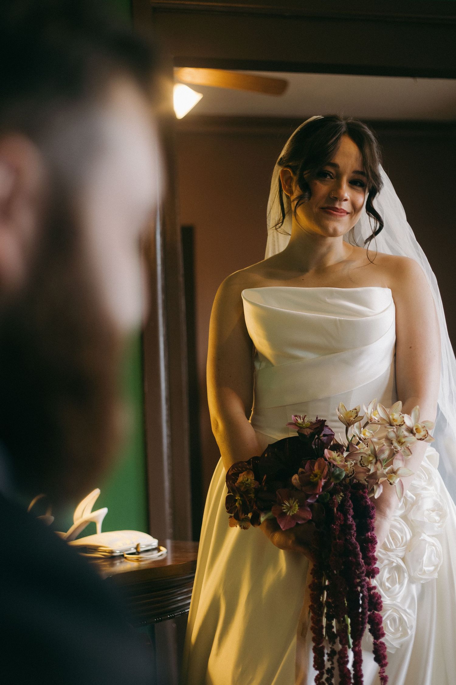 Elegant white wedding dress illuminated by warm light with cascading floral bouquet details.