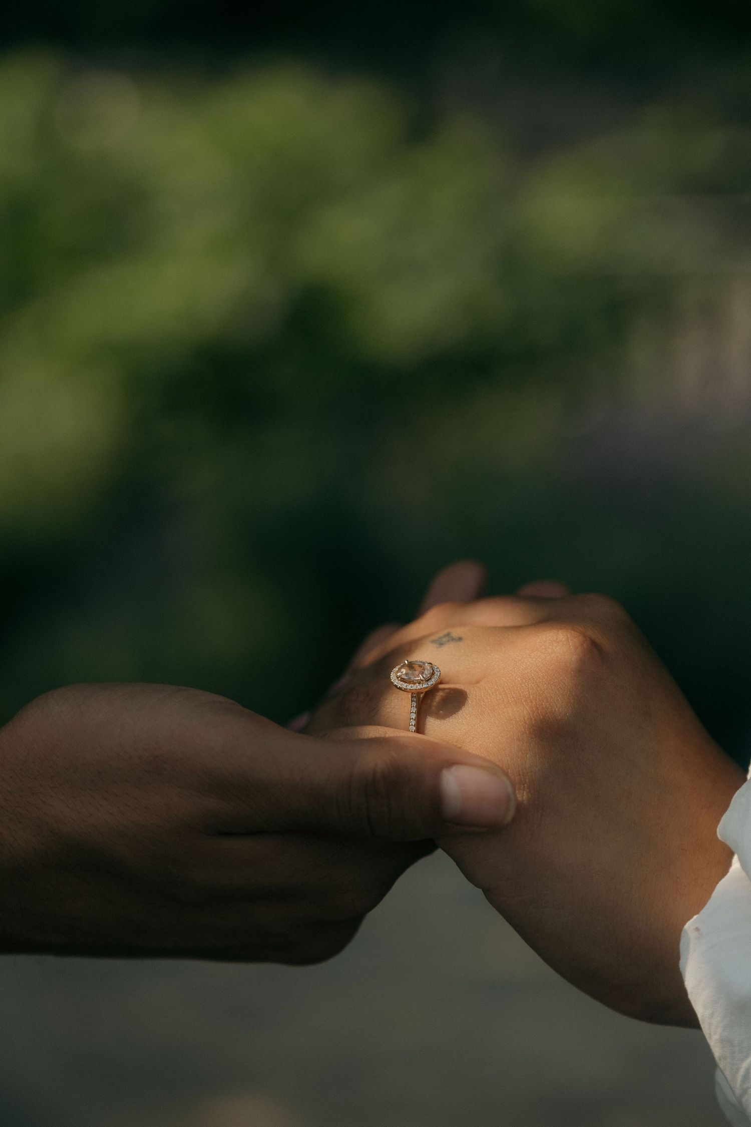 Close-up of two hands holding together with a delicate diamond engagement ring in soft natural light.