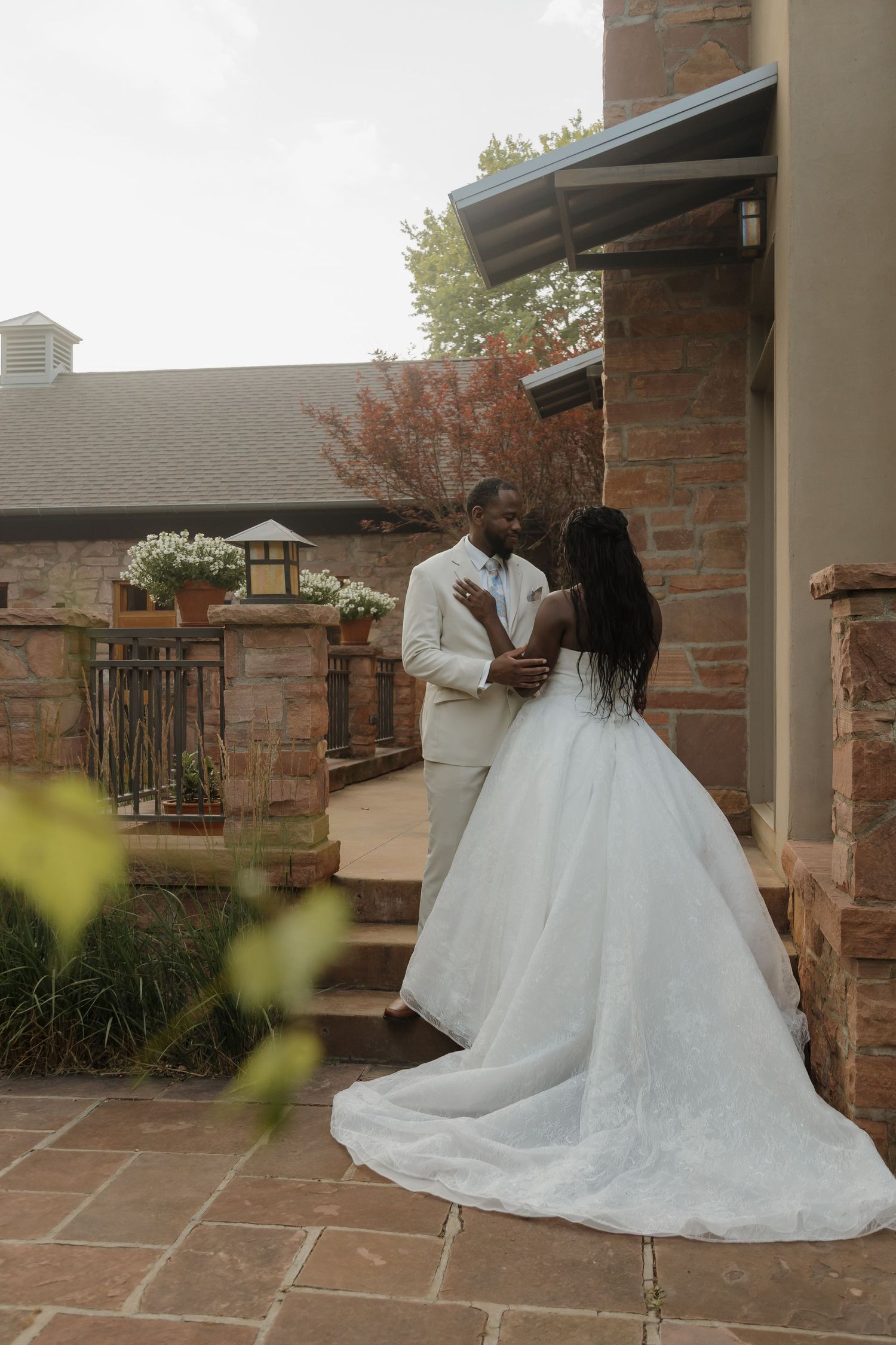 Black bride and groom share a tender embrace on a stone patio outside a rustic wedding venue.