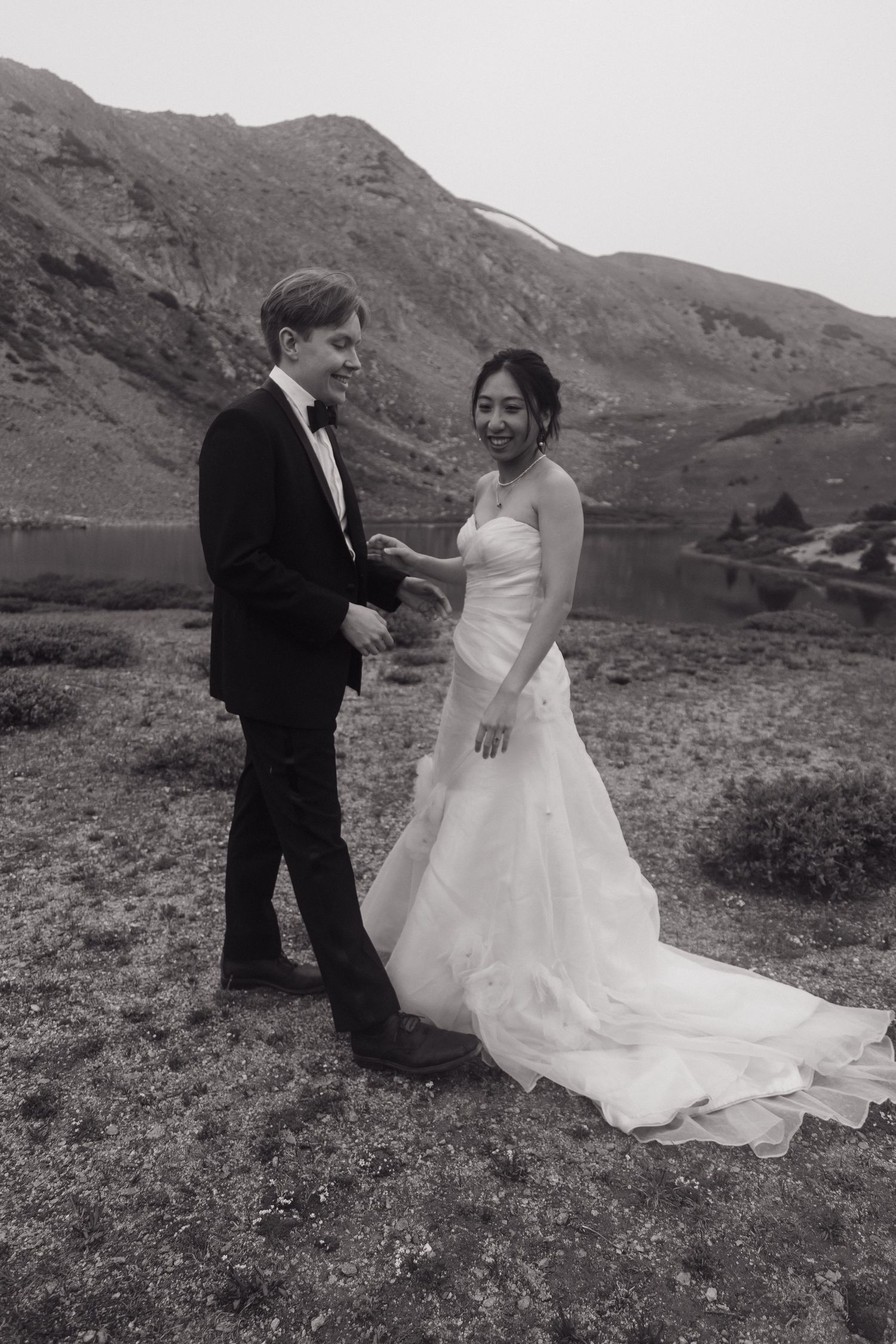 Black and white portrait of bride and groom holding hands and smiling beside a mountain lake elopement.