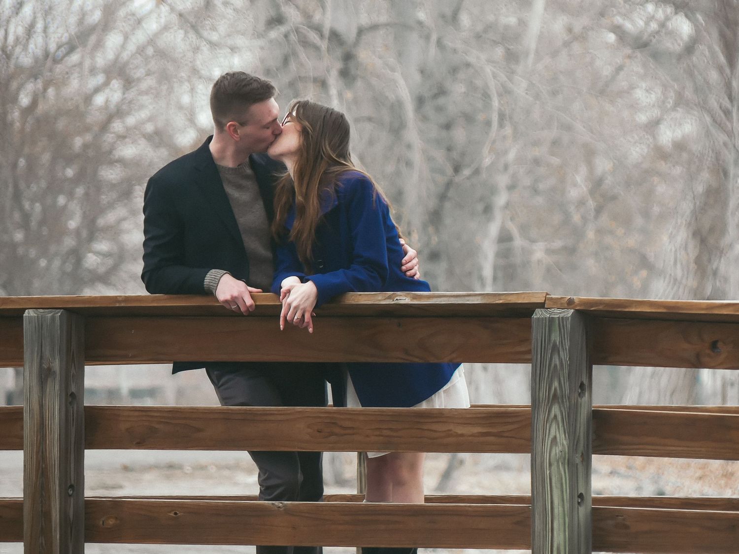 Two people sharing an intimate moment on a wooden bridge in a winter setting.