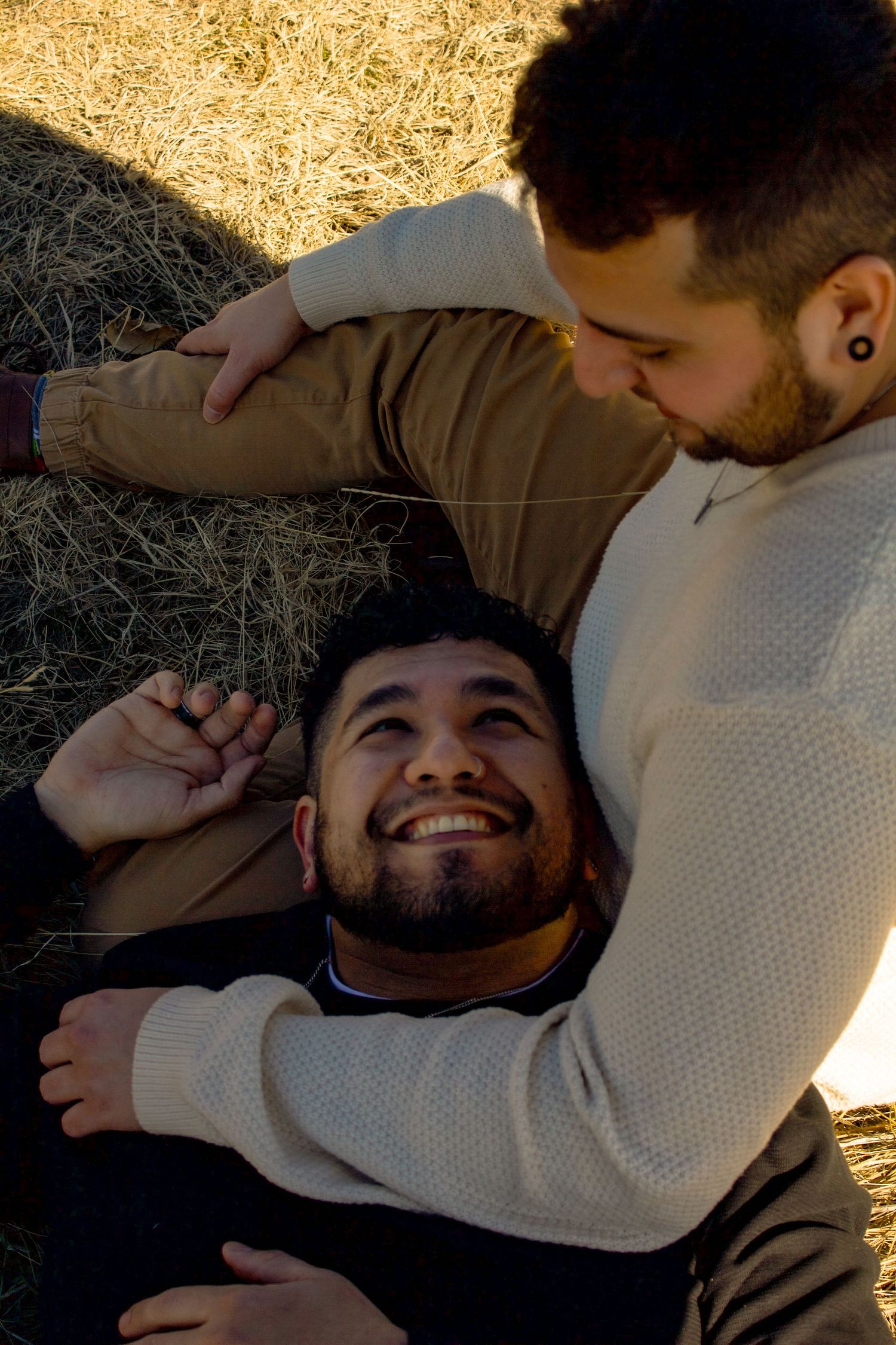 Two people share a tender moment while relaxing in grass during golden hour.