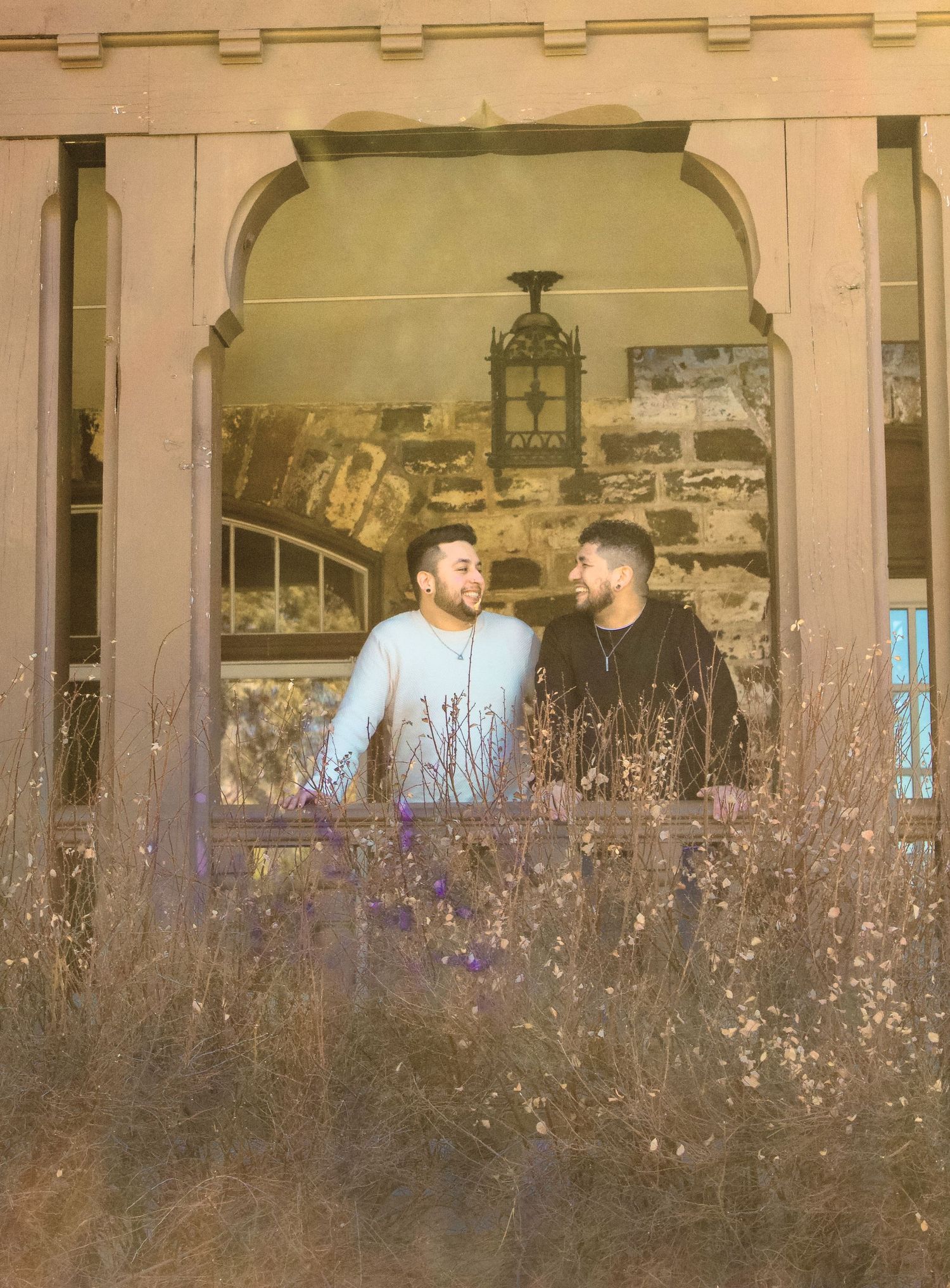 Two people sharing a moment through an arched doorway surrounded by dried plants.