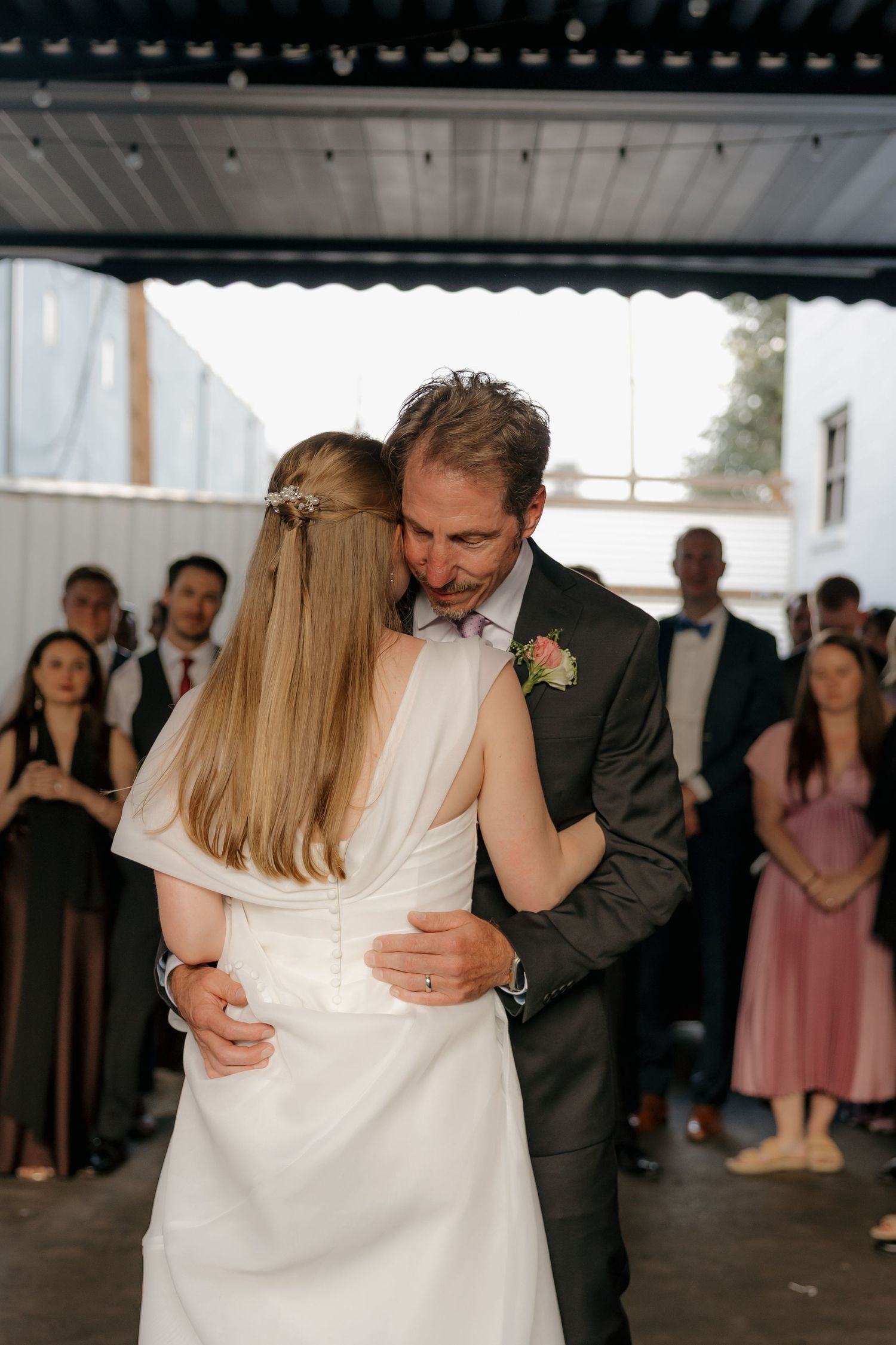 Bride and groom share intimate first dance embrace surrounded by wedding reception guests.