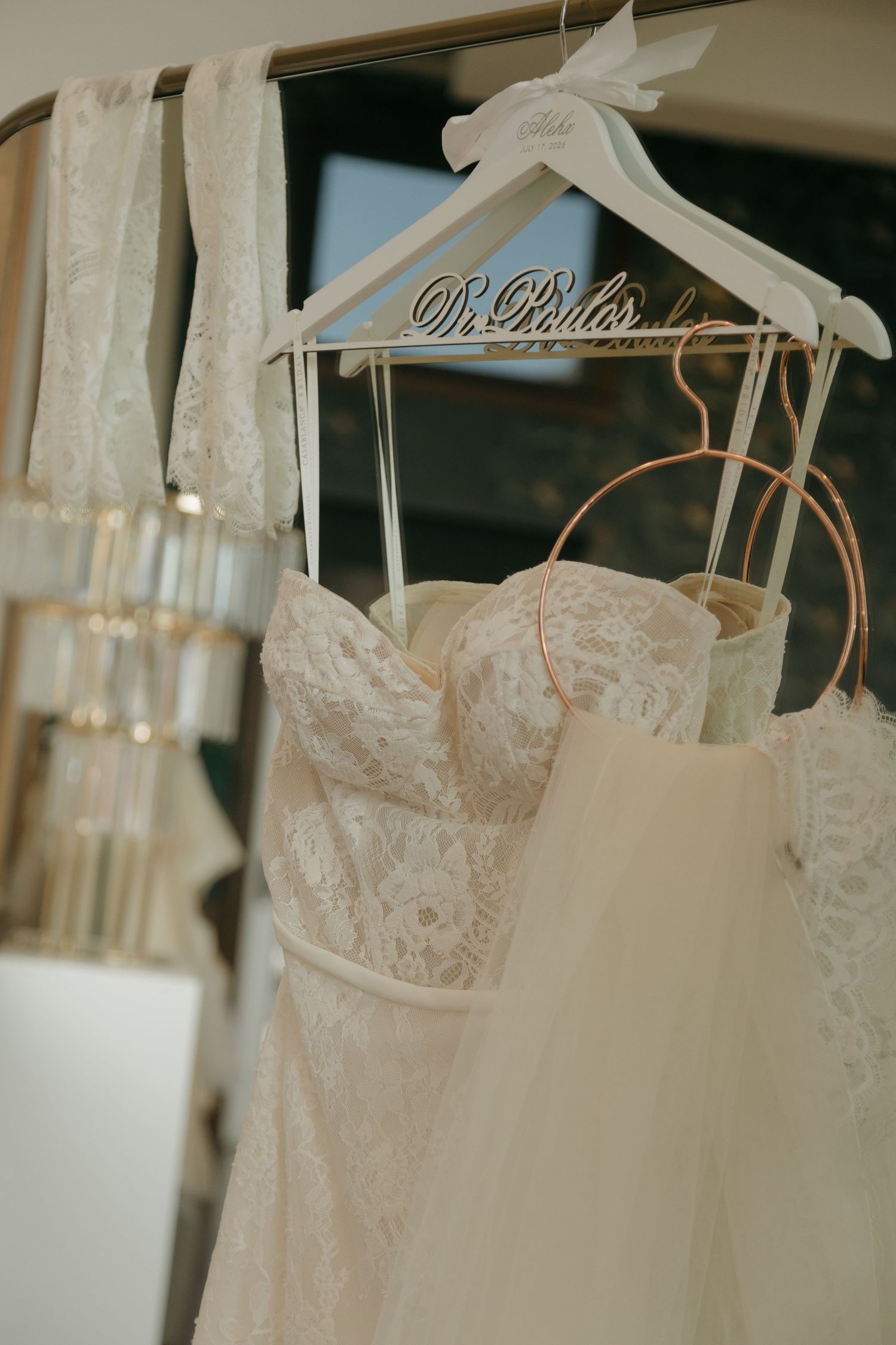 Elegant lace wedding dress hanging on a decorative Mr. & Mrs. hanger in a bridal suite.