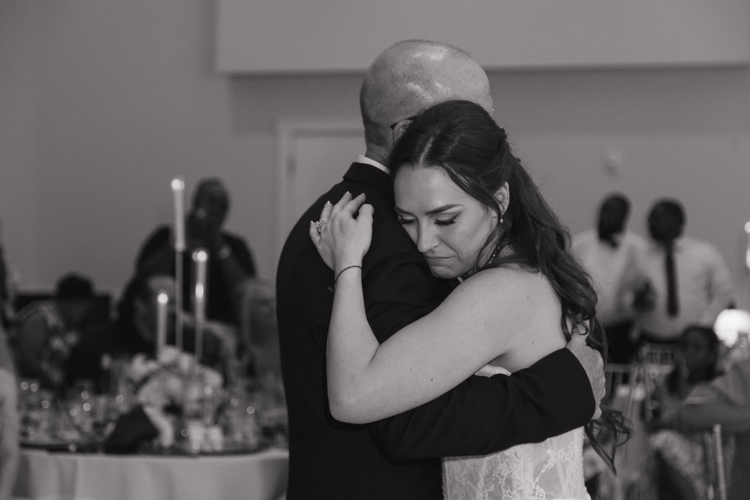 Emotional bride sharing a slow dance with father during wedding reception in black and white.