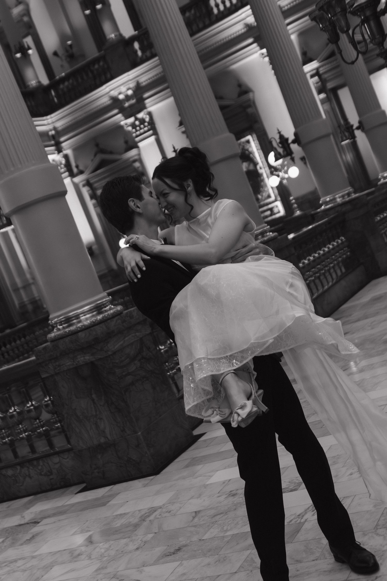 A couple dancing together in black and white on a grand ballroom floor.