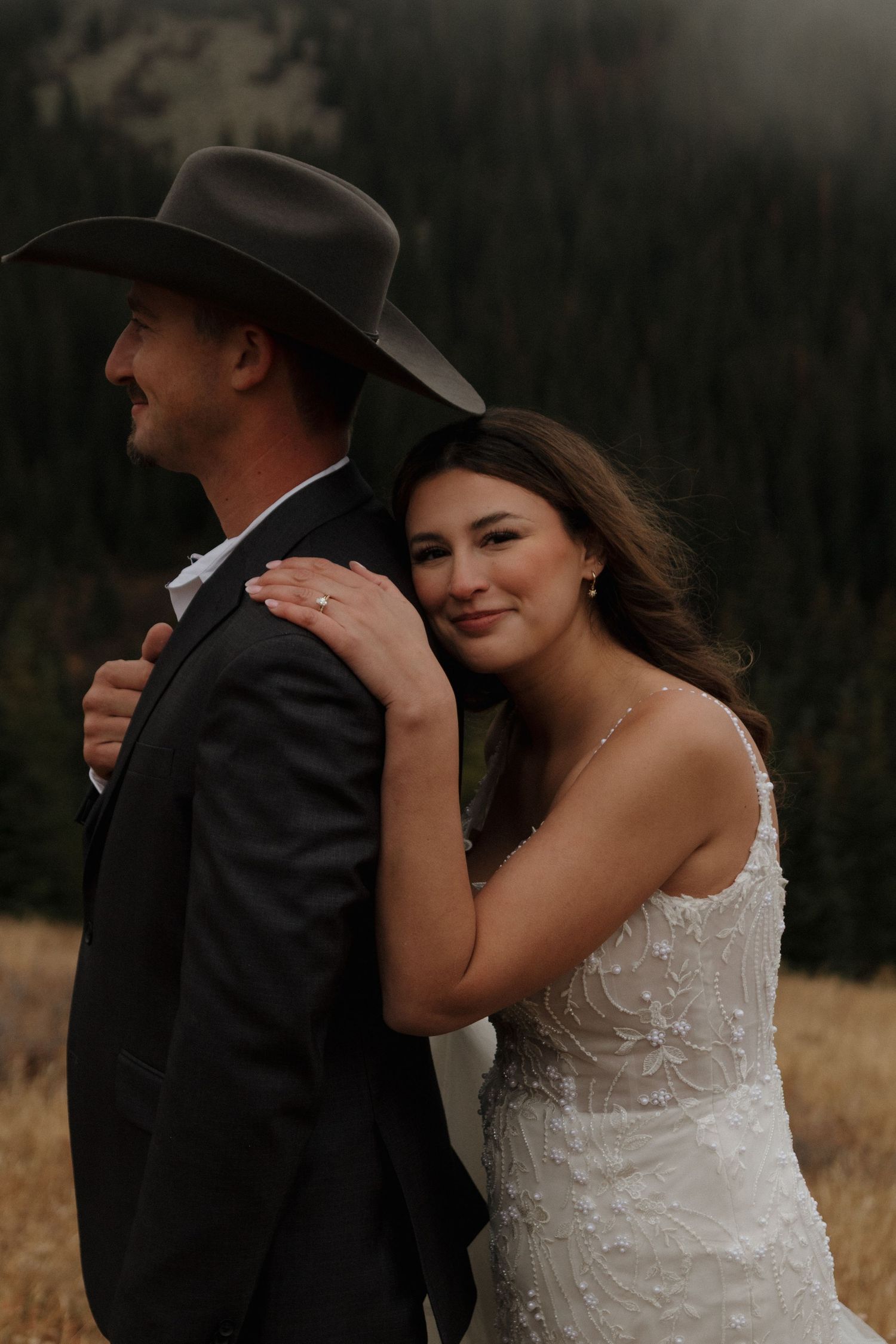 A wedding couple poses together in a rustic outdoor setting with mountains in the background.