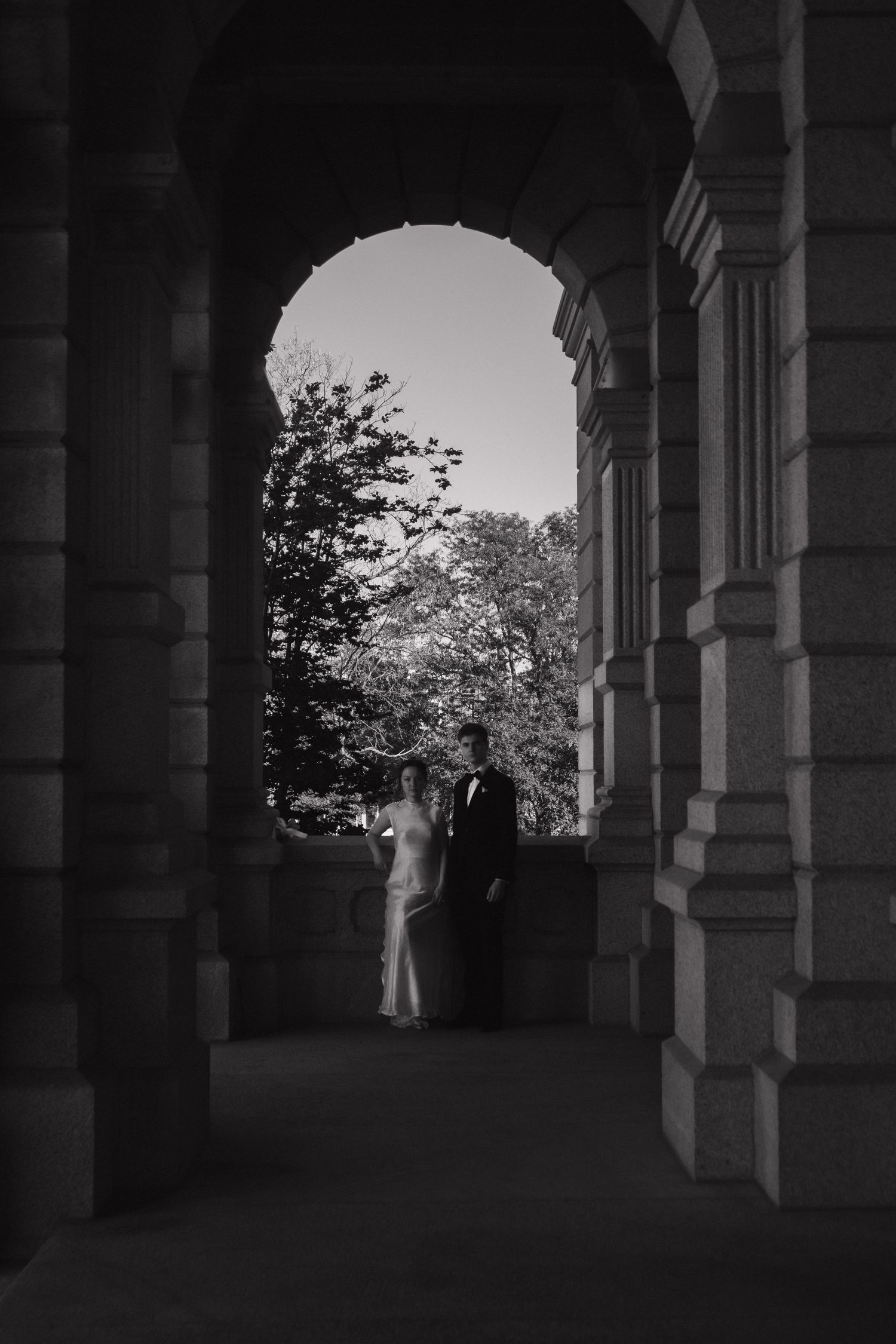 A black and white photograph showing a columned walkway with arched architecture casting dramatic shadows.