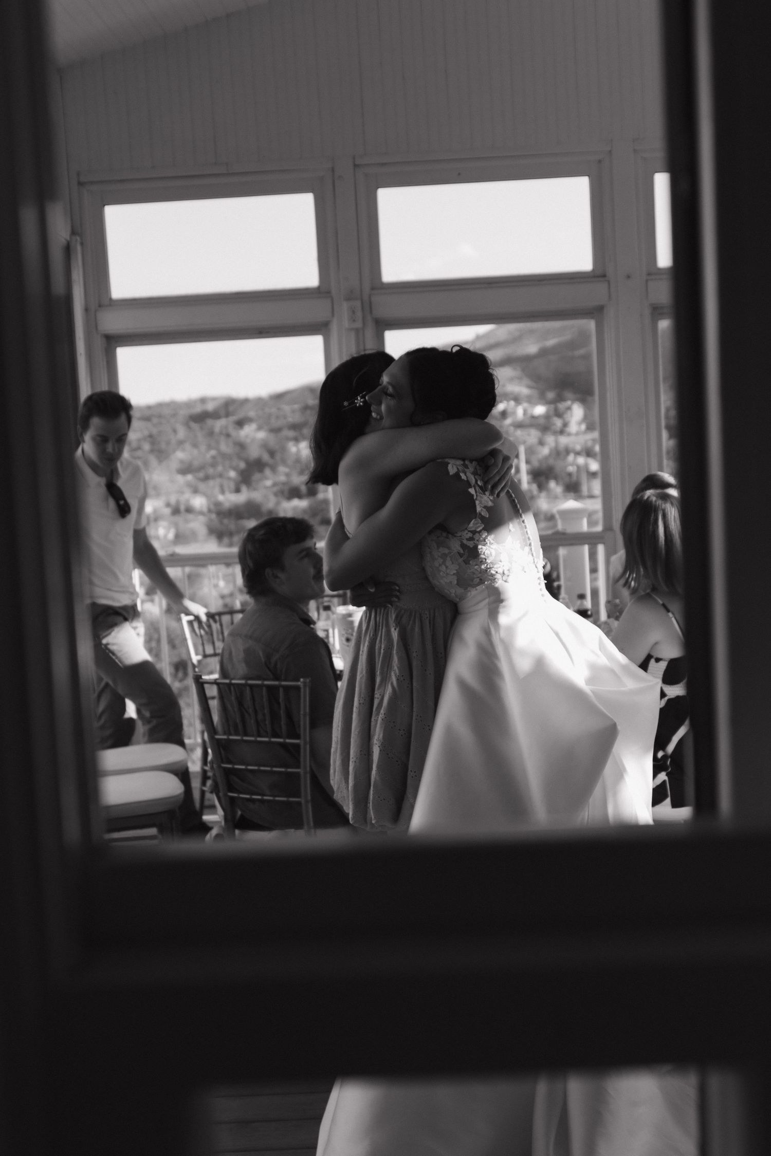 Black and white candid shot of wedding reception through venue windows.