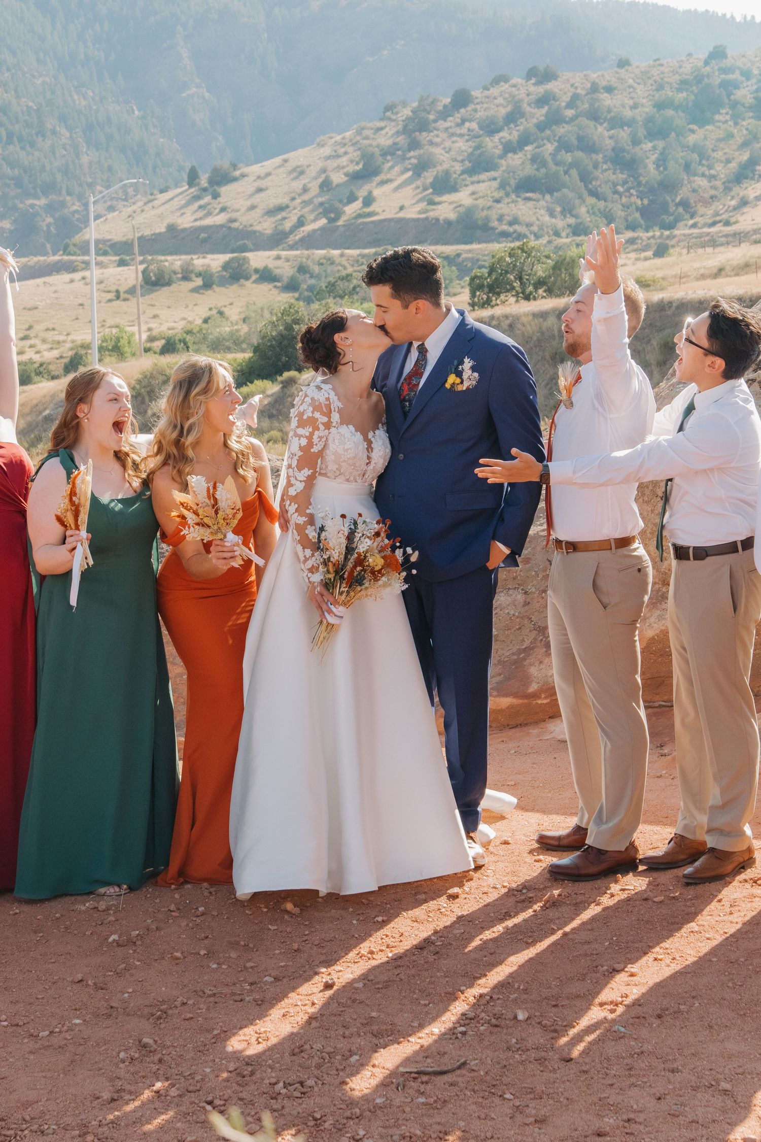 Wedding party in colorful dresses and suits lines up for photos on red desert terrain.