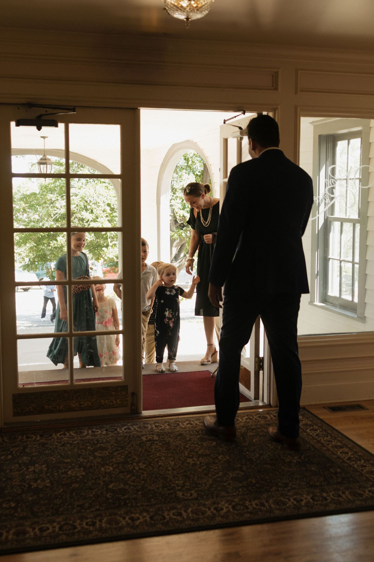 Wedding attendees gather in an elegant room with large windows and chandelier.