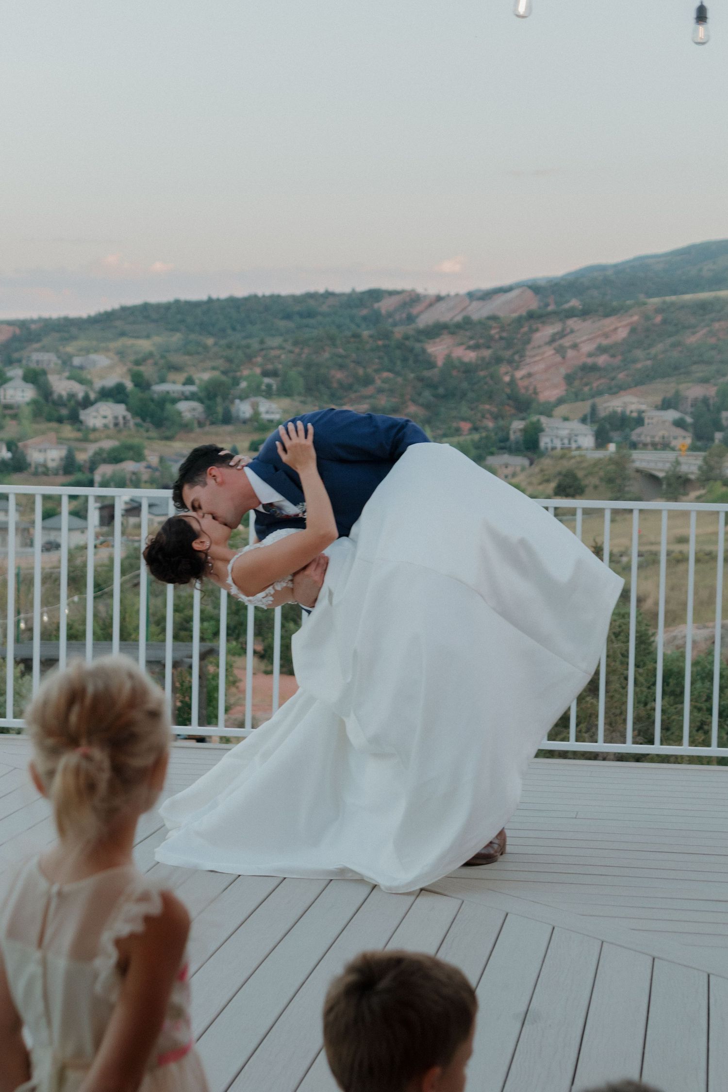 Wedding couple performing a dramatic dip on an outdoor deck with mountain views.