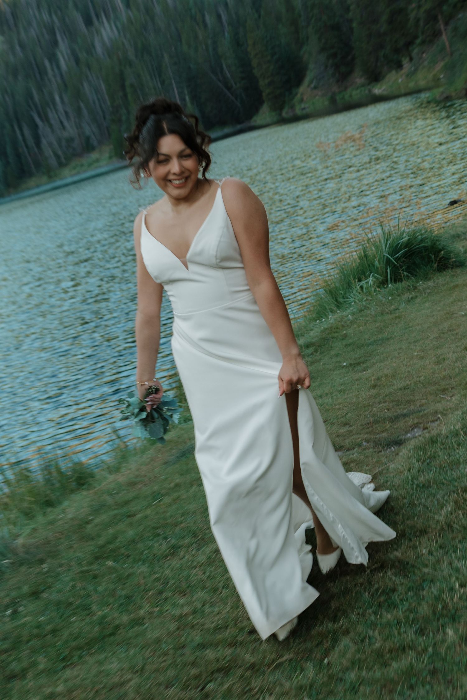 A figure in a flowing white dress twirls playfully by a serene mountain lake.