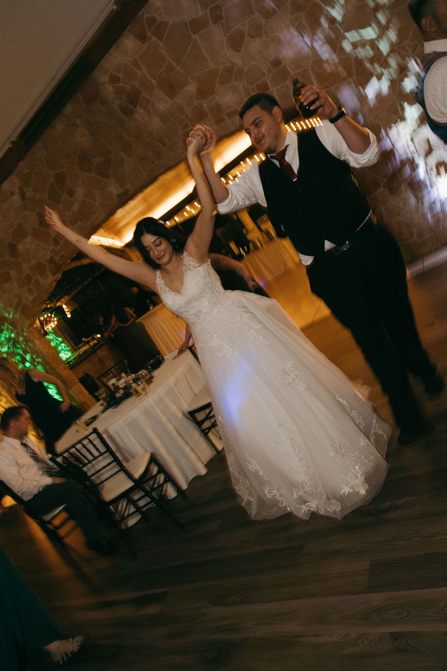 Bride and groom dance together energetically raising their arms on the wedding reception dance floor.