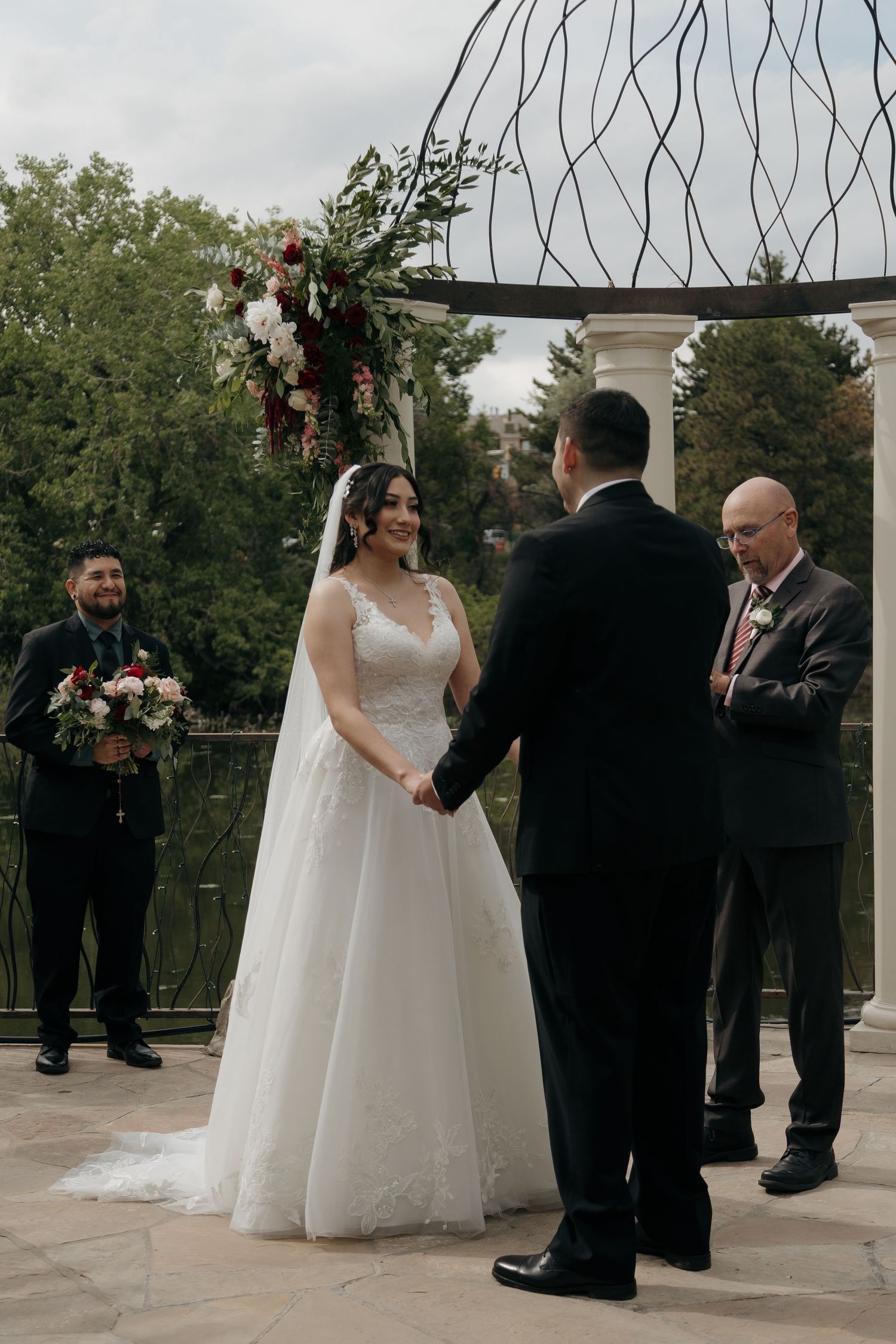 Bride in lace gown and groom holding hands at outdoor wedding ceremony altar.