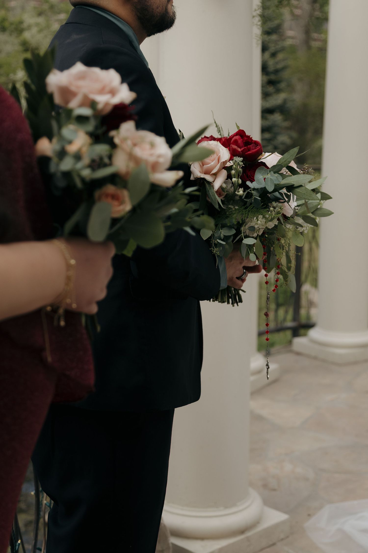 Wedding party members holding bouquets of pink and red roses with eucalyptus greenery.