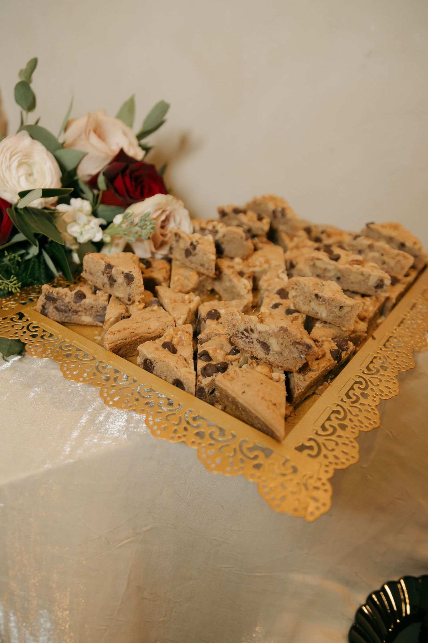 Chocolate chip cookie bars displayed on gold tray with floral arrangement at wedding.