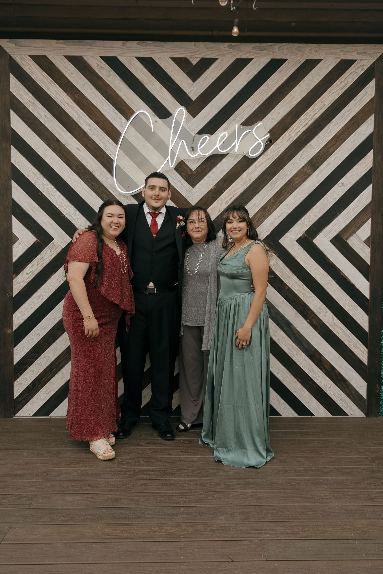 Group of four wedding guests posing in front of black and white geometric Cheers backdrop.