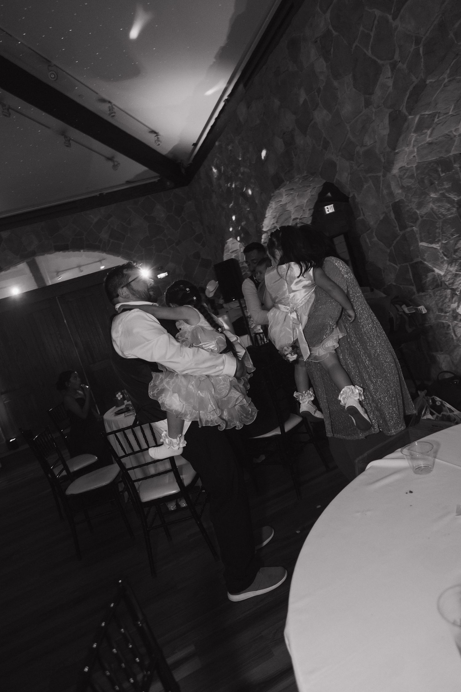 Black and white candid photo of wedding guests dancing and celebrating energetically at the reception.