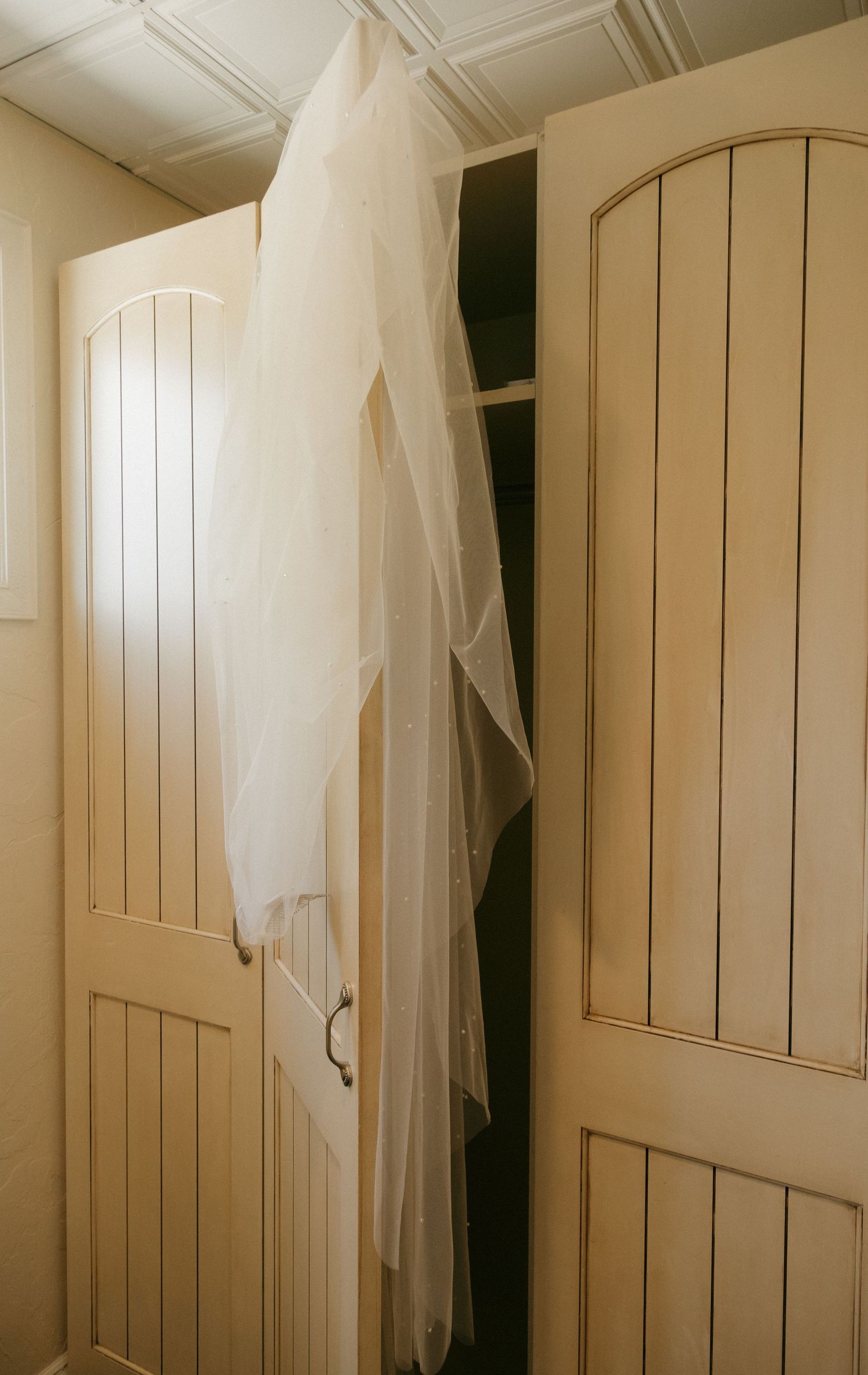 White wedding veil draped over cream wooden cabinet doors in a bridal preparation room.