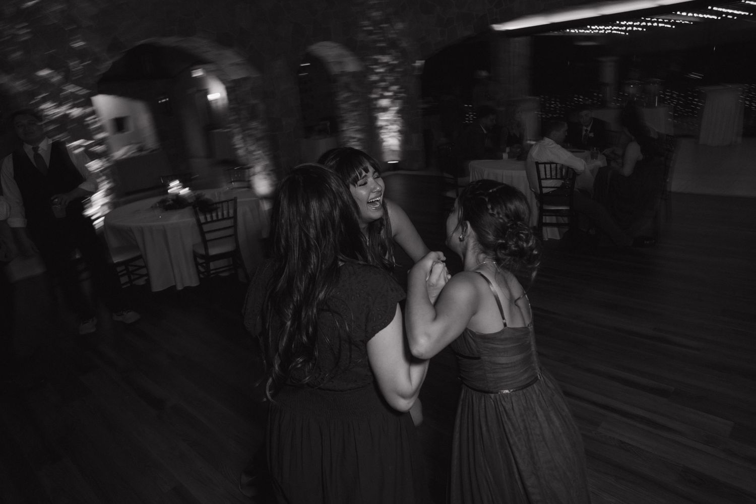 Black and white photo of two women in formal gowns dancing together at a wedding reception.