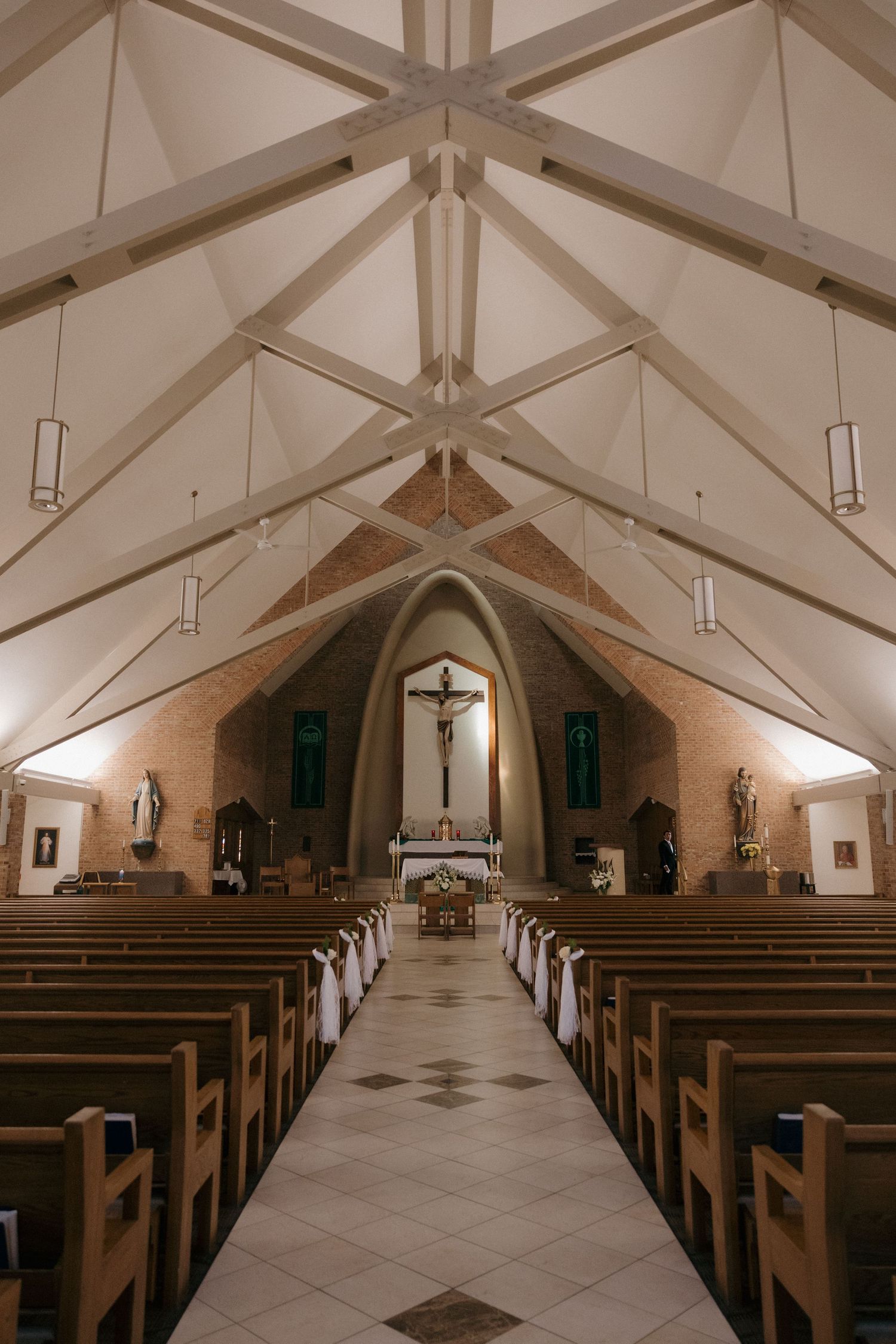 Interior of a Catholic church with wooden pews, vaulted white ceiling beams, and crucifix above the altar.