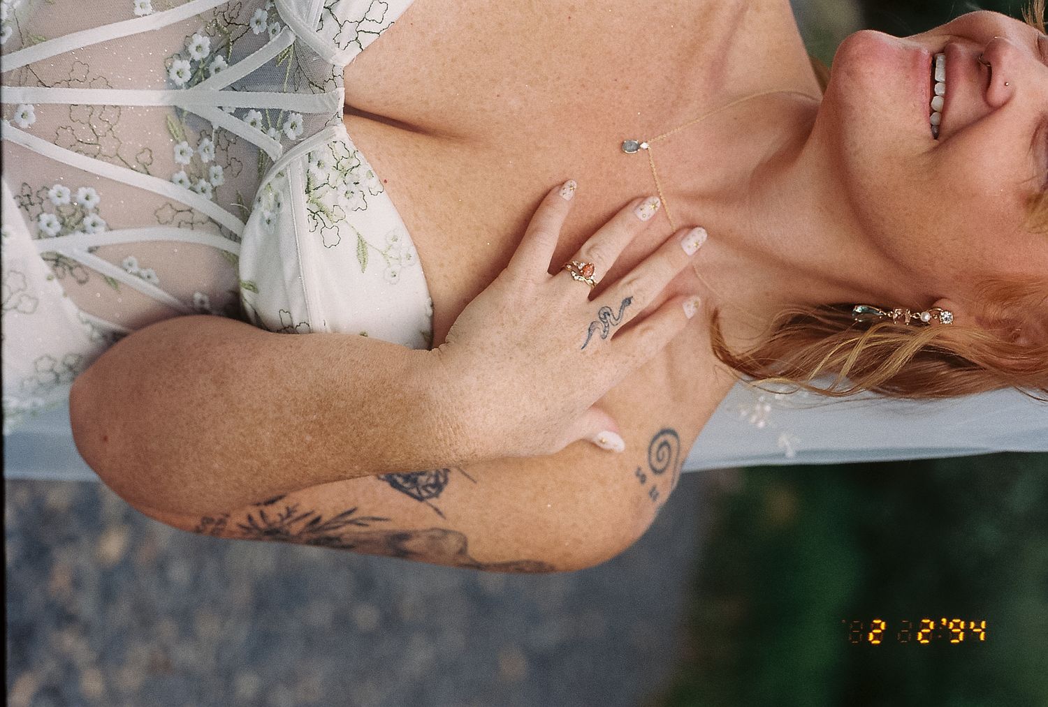 Close-up of laughing bride in lace wedding dress with spiral tattoo and delicate ring on hand.